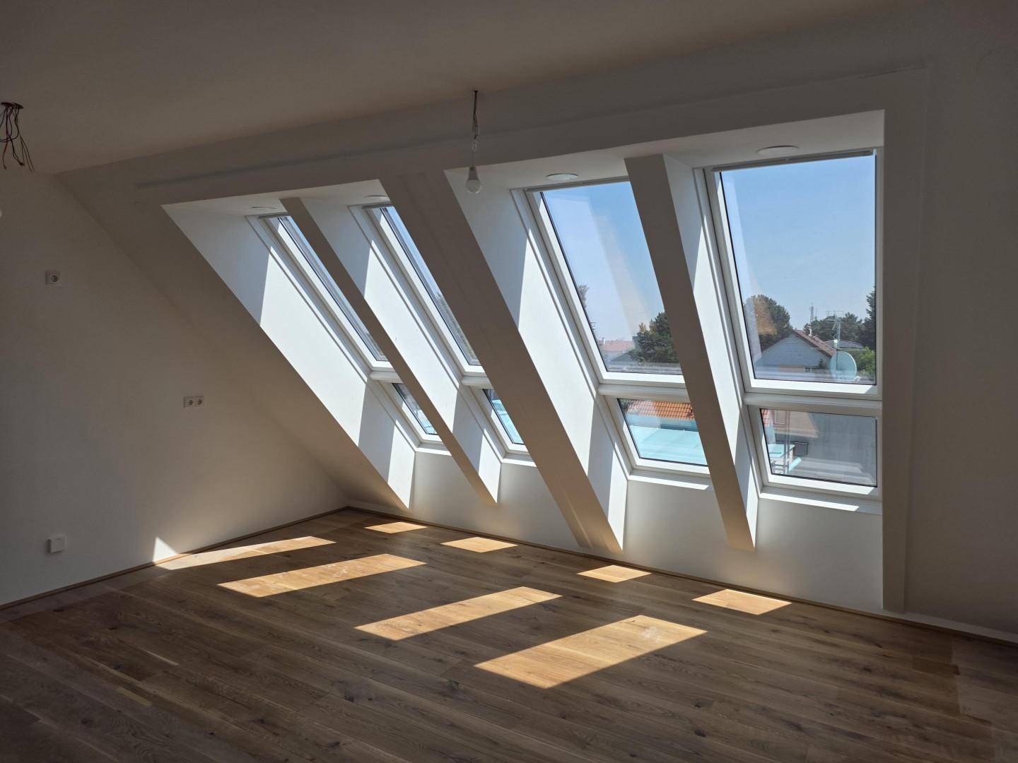 Lichtdurchflutetes Dachgeschosszimmer mit Holzboden und mehreren schrägen Dachfenstern.
