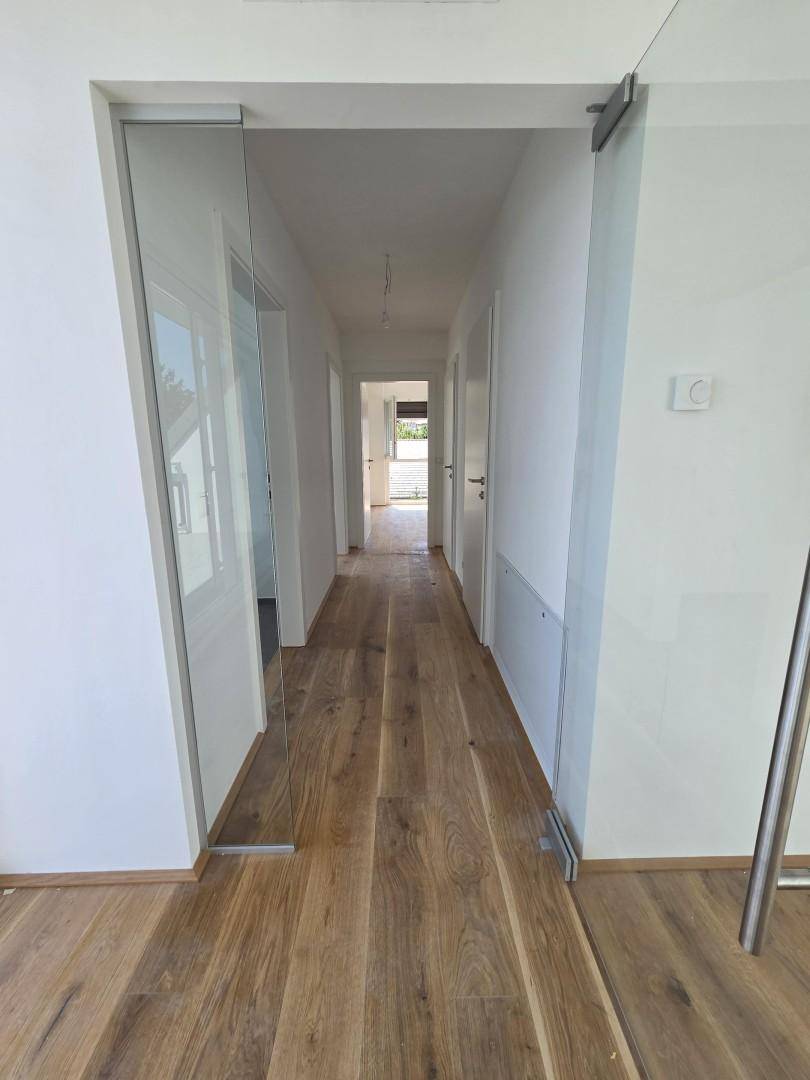 Langer, heller Flur mit Holzboden und modernen Glastüren, der verschiedene Bereiche verbindet.
