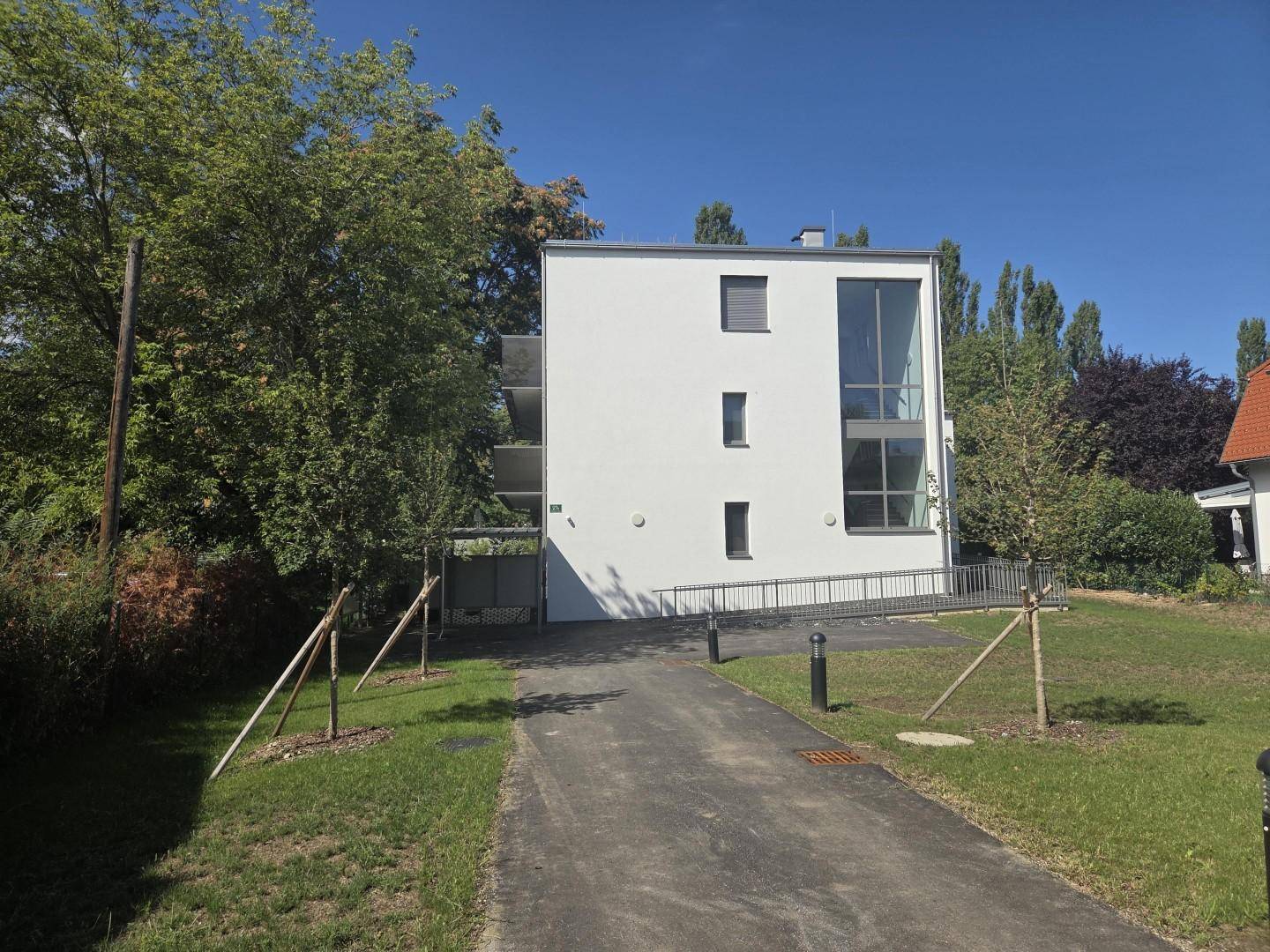 Moderne Gebäudefassade mit großen Fenstern und grüner Umgebung.