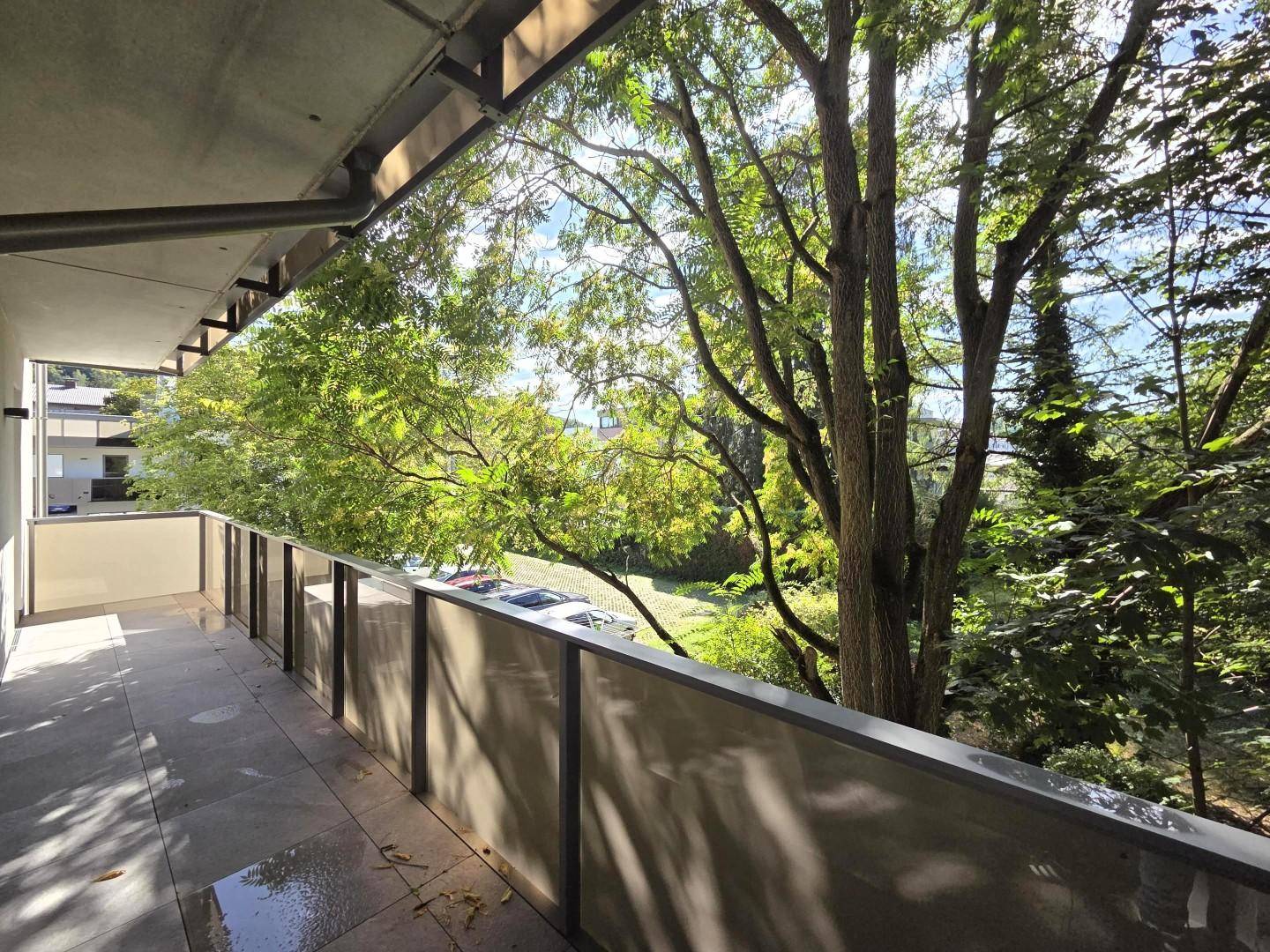 Geräumiger Balkon mit Fliesenboden und Blick ins Grüne, umgeben von Bäumen.