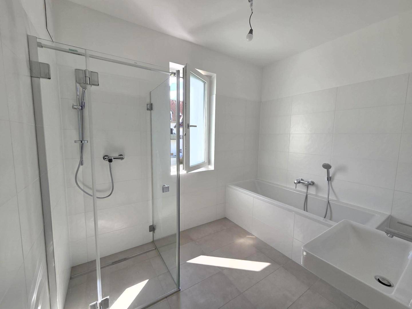 Helles, modernes Badezimmer mit Dusche, Badewanne und Fenster.