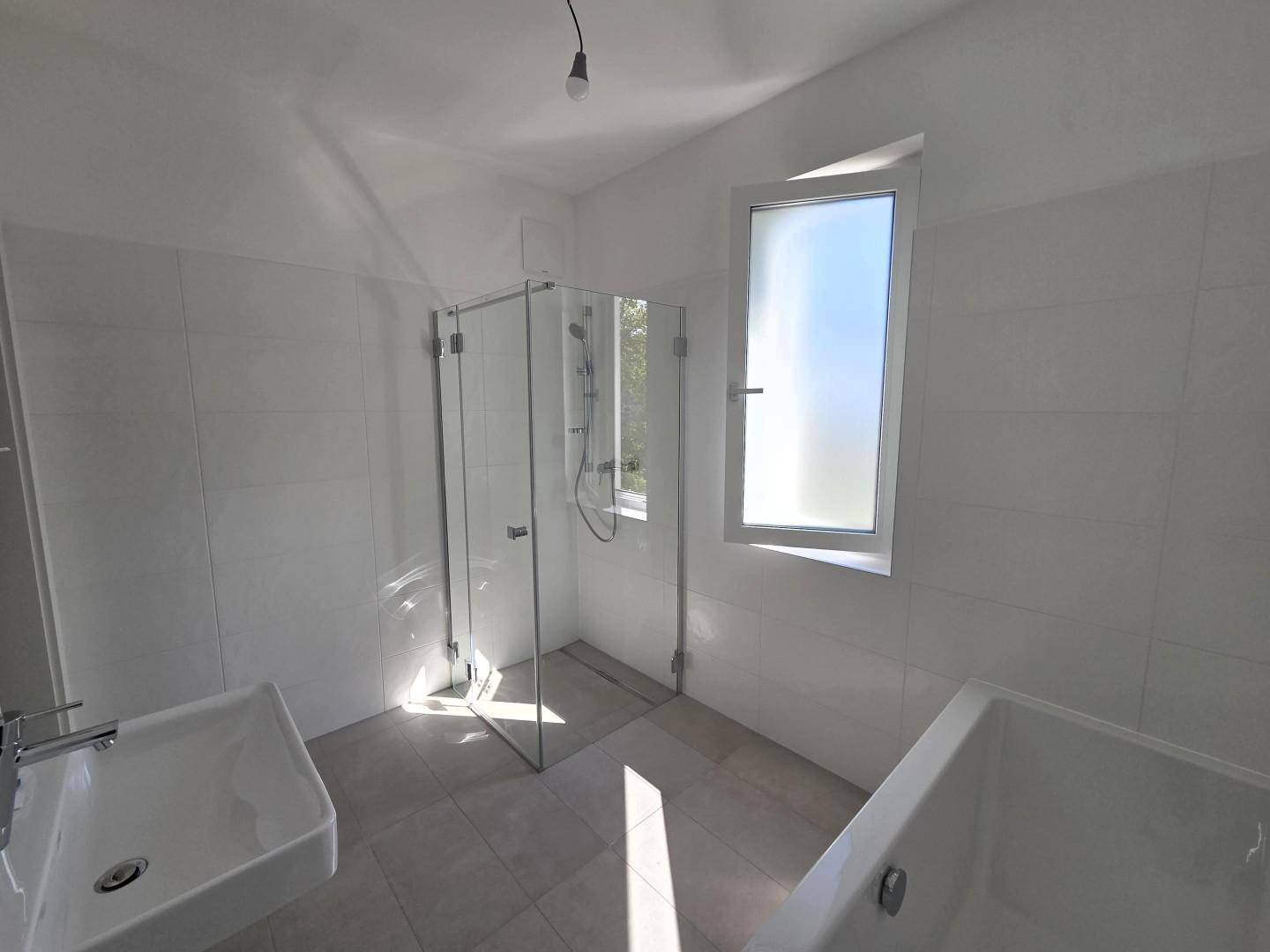 Modernes Badezimmer mit bodengleicher Dusche, Badewanne und mattiertem Fenster.