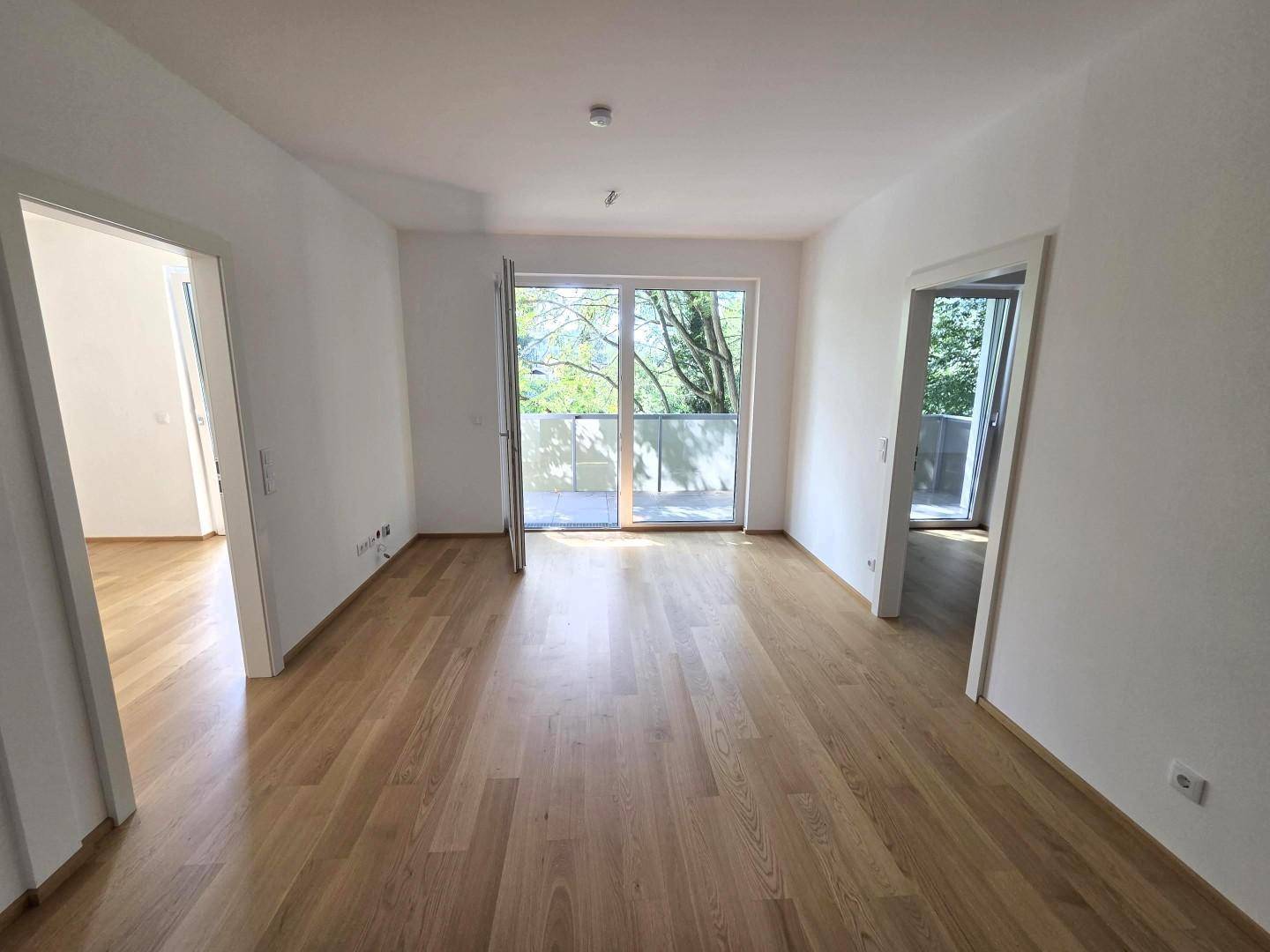 Geräumiges Wohnzimmer mit hellem Parkettboden und Zugang zum Balkon.