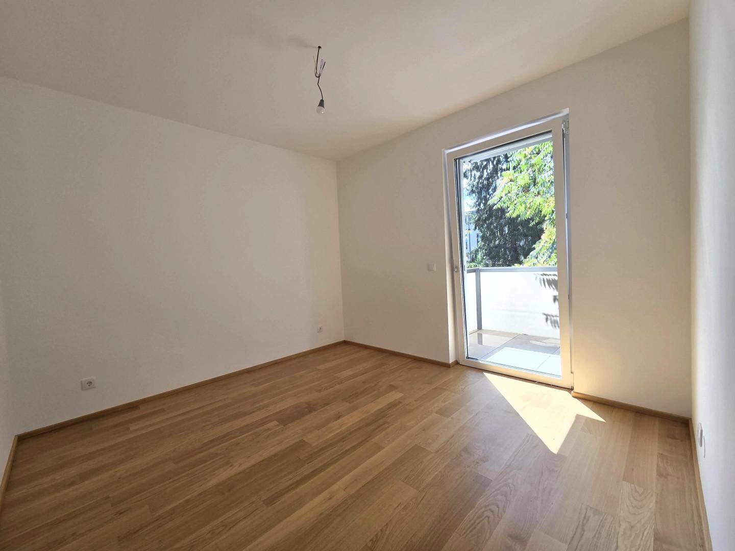 Helles Schlafzimmer mit Holzboden und großem Fenster mit Balkonzugang.