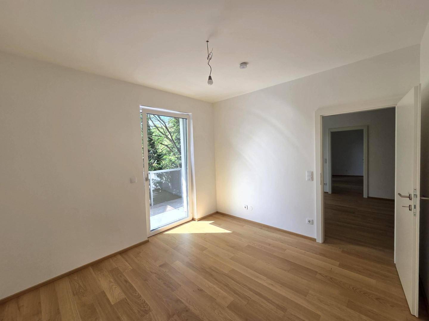 Schlafzimmer mit Parkettboden und Zugang zu einem Balkon, viel Tageslicht.