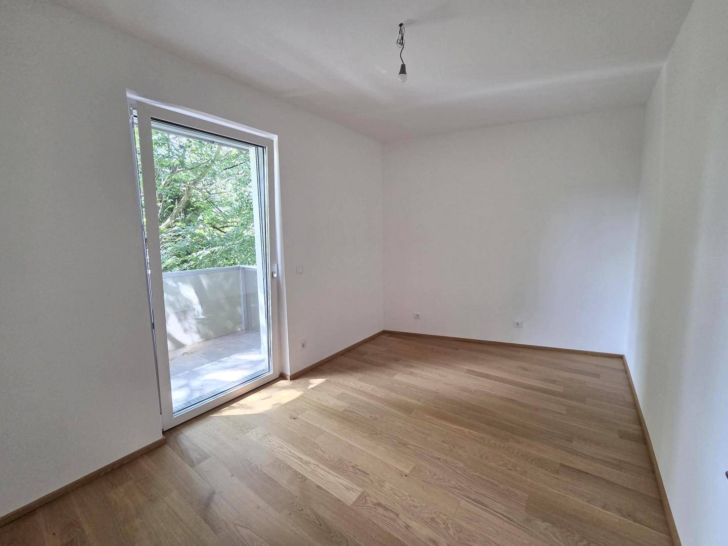 Geräumiges Schlafzimmer mit Holzboden und Balkontür, ideal für natürliche Belüftung.