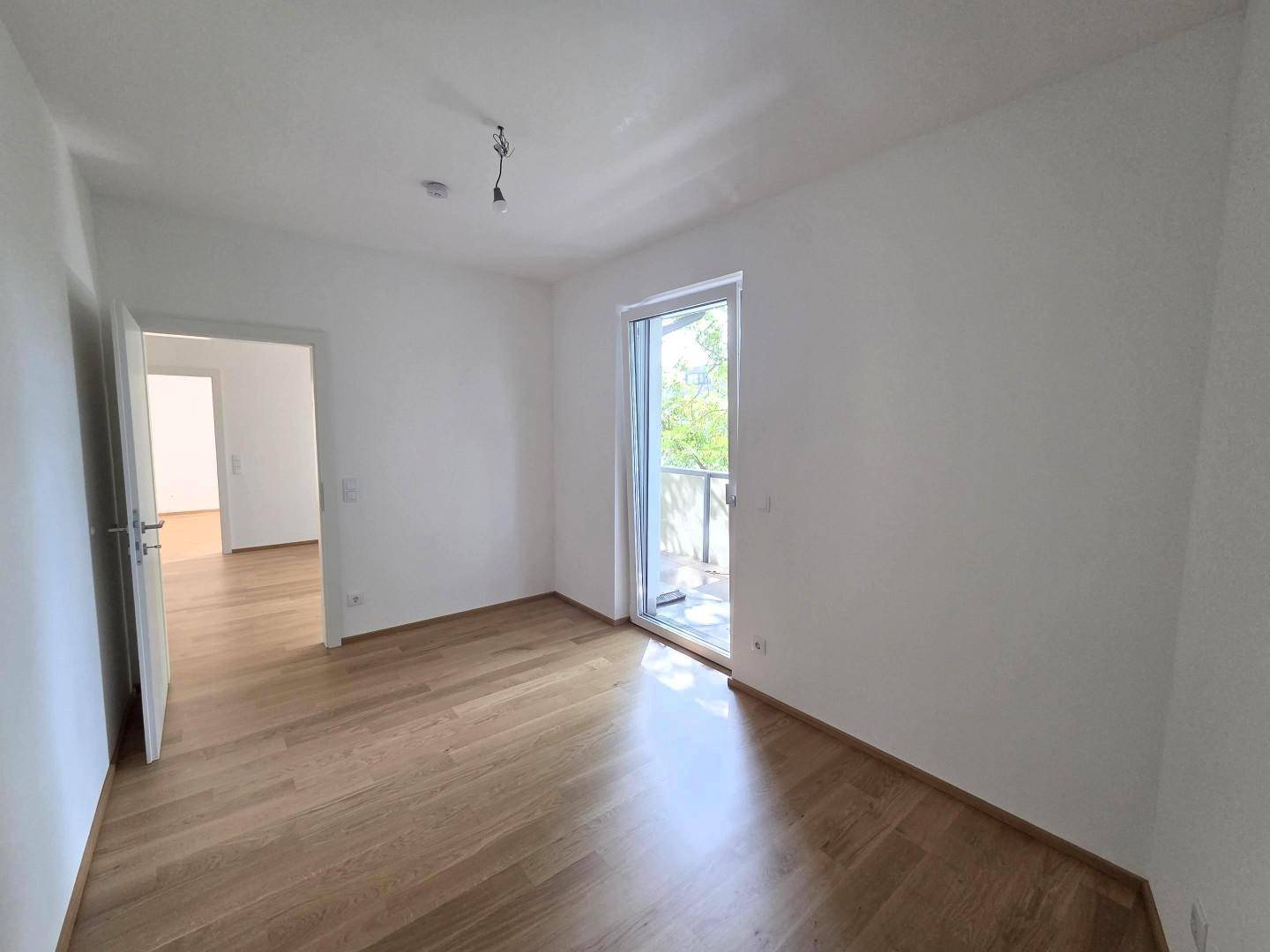 Helles Schlafzimmer mit Parkettboden und Zugang zu einem weiteren Raum.