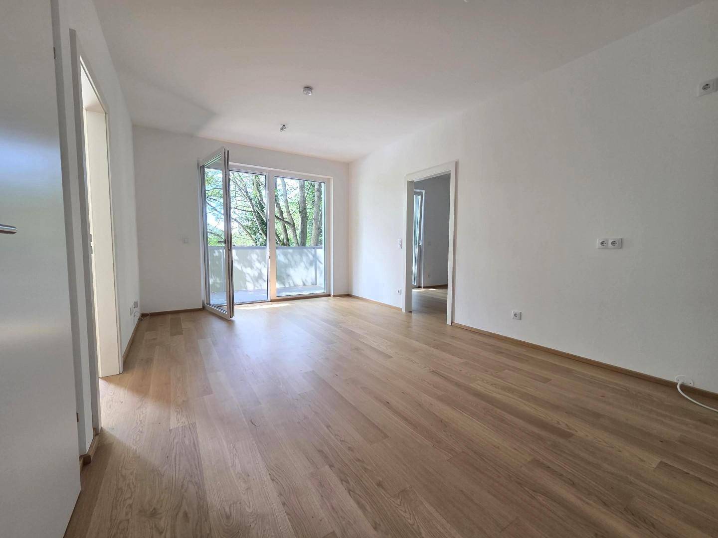 Heller Wohnbereich mit Parkettboden und großen Fenstern zum Balkon.