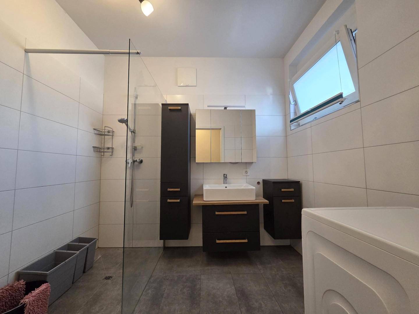 Modernes Badezimmer mit ebenerdiger Dusche, Einzelwaschbecken und Waschmaschinenanschluss.