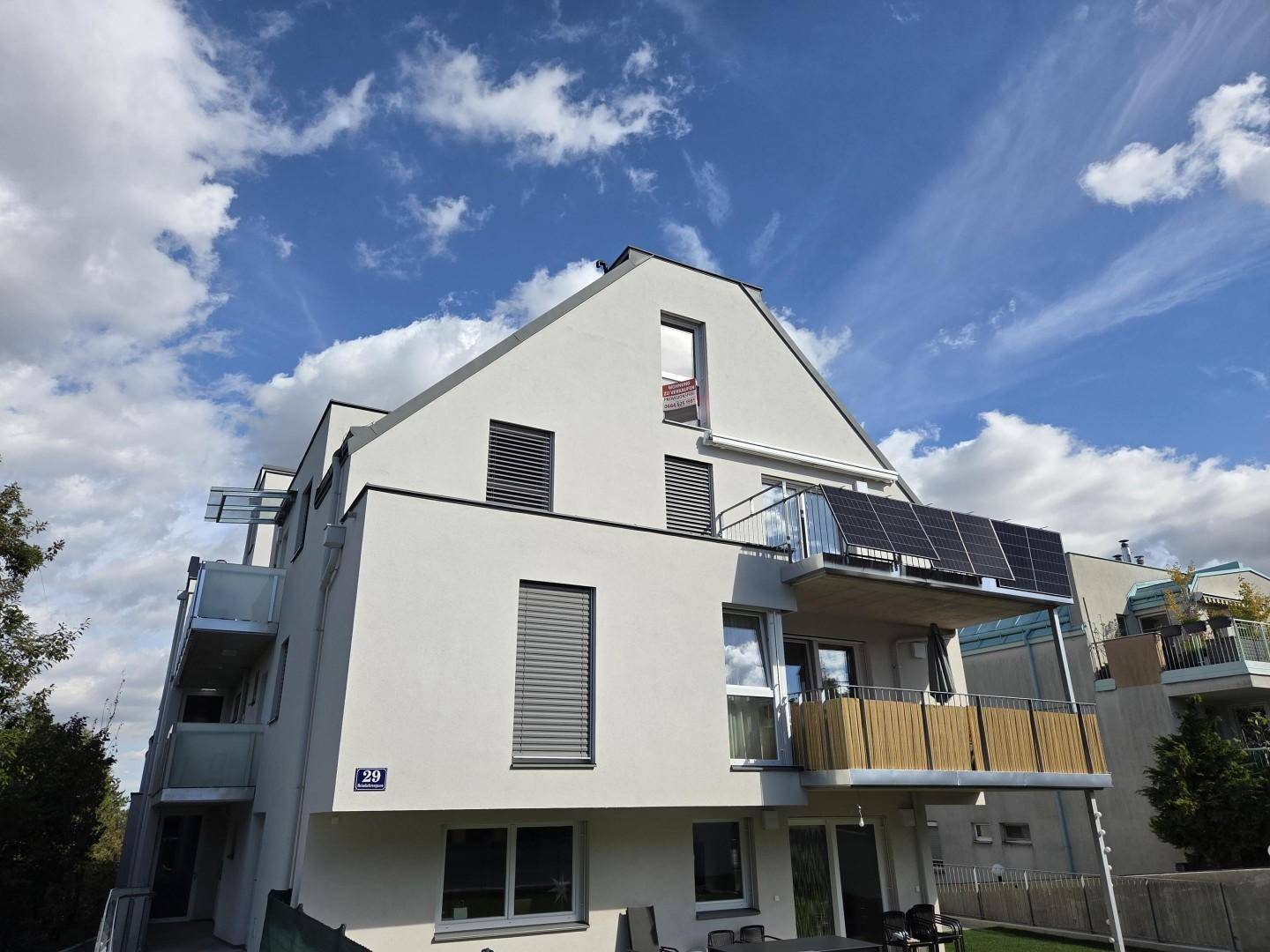 Modernes Mehrfamilienhaus mit Balkonen, Rollläden und Photovoltaikanlage auf dem Dach.