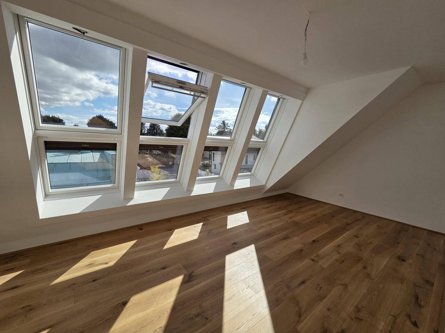 Heller Raum mit Holzboden und einer Reihe von Dachfenstern, die den Raum mit Licht füllen.