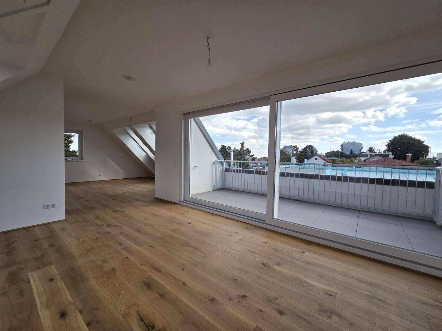 Offener Wohnbereich mit Holzboden, Zugang zum Balkon und zusätzlichen Dachfenstern.