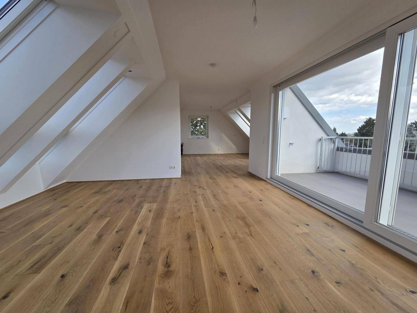 Heller Wohnraum mit Holzboden, großen Fenstern und Zugang zu einem sonnigen Balkon.