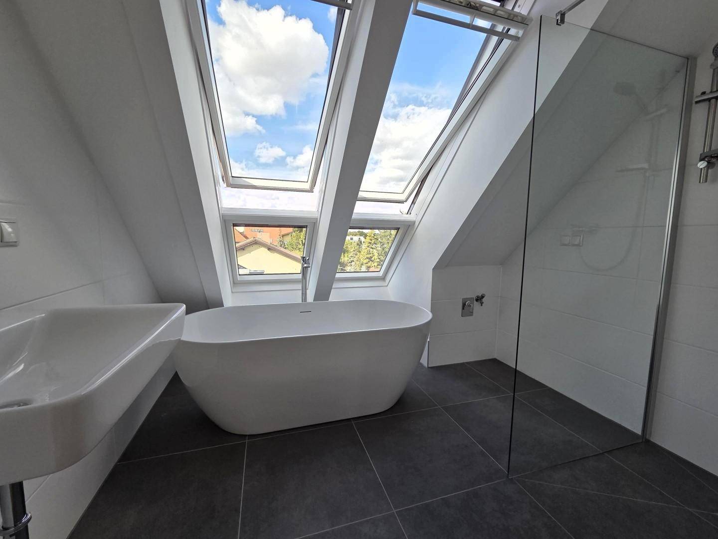 Modernes Badezimmer mit freistehender Badewanne, Glasdusche und Dachfenstern.