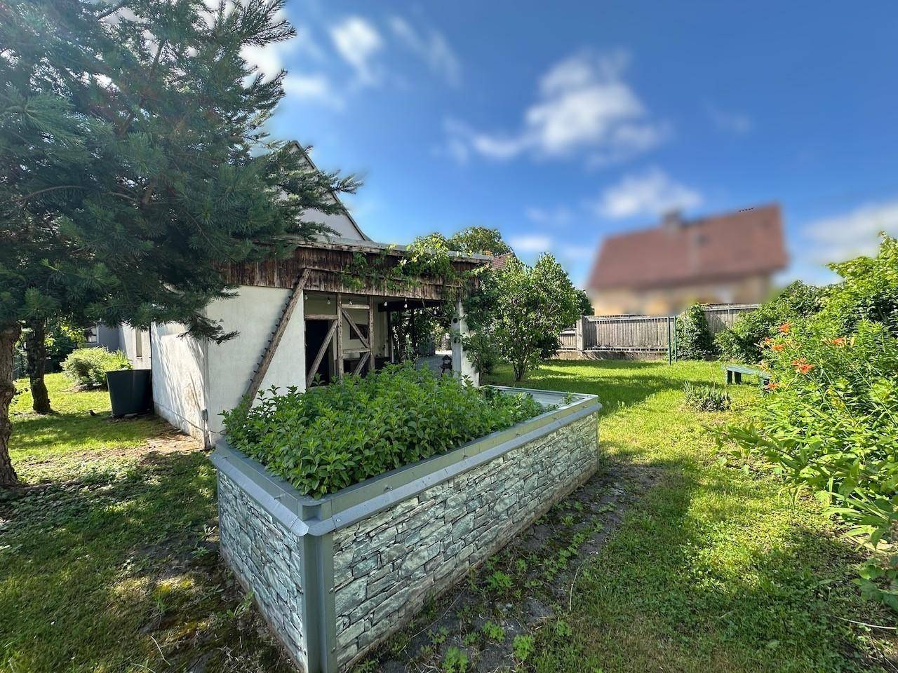 Gepflegter Gartenbereich mit einem Hochbeet und viel Grün unter einem strahlend blauen Himmel.