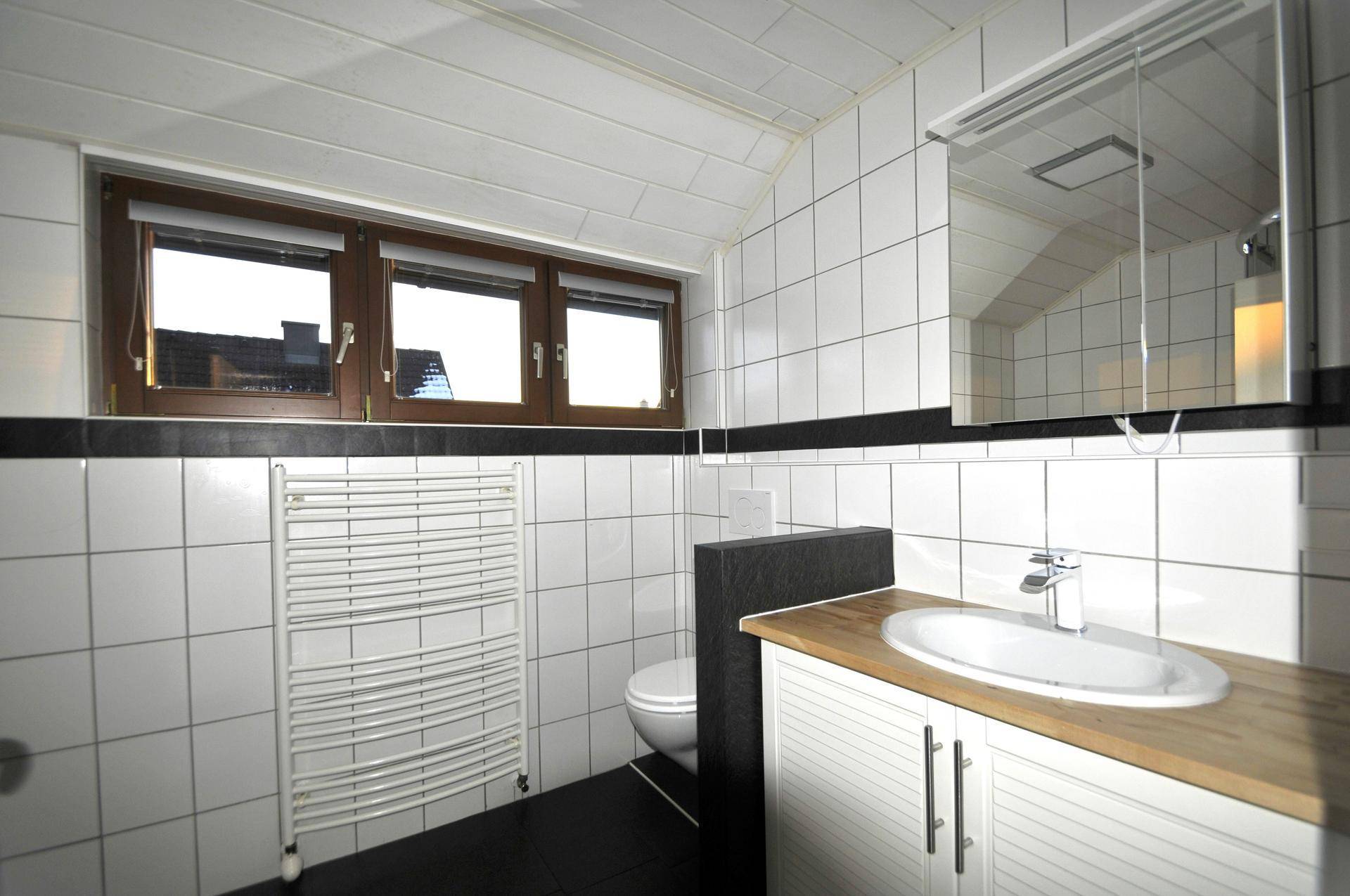 Helles Badezimmer mit Fenster, weißen Fliesen und beheiztem Handtuchhalter.