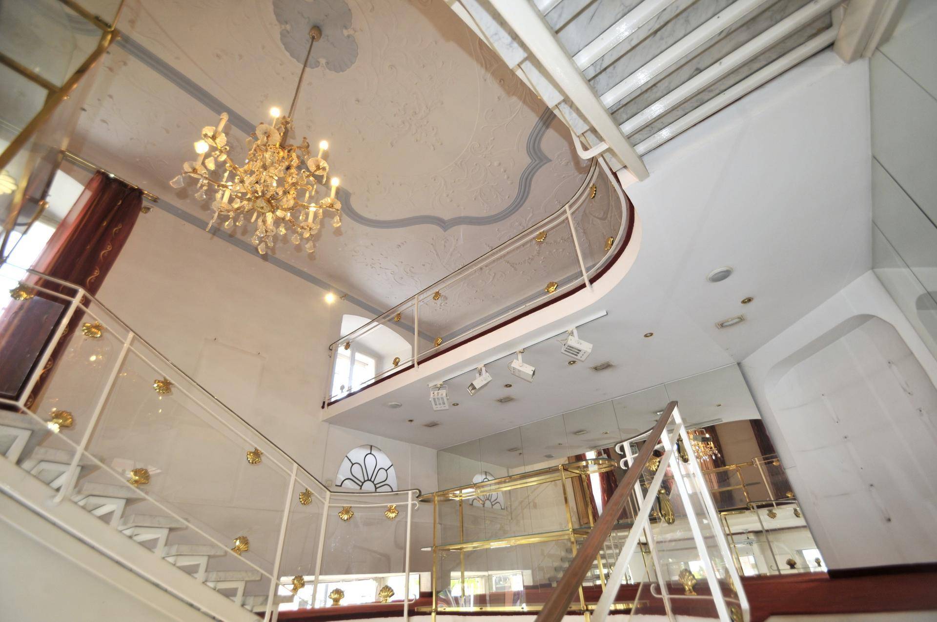 Elegante Treppe mit Glasgeländer und einem prunkvollen Kronleuchter im oberen Bereich des Raumes.