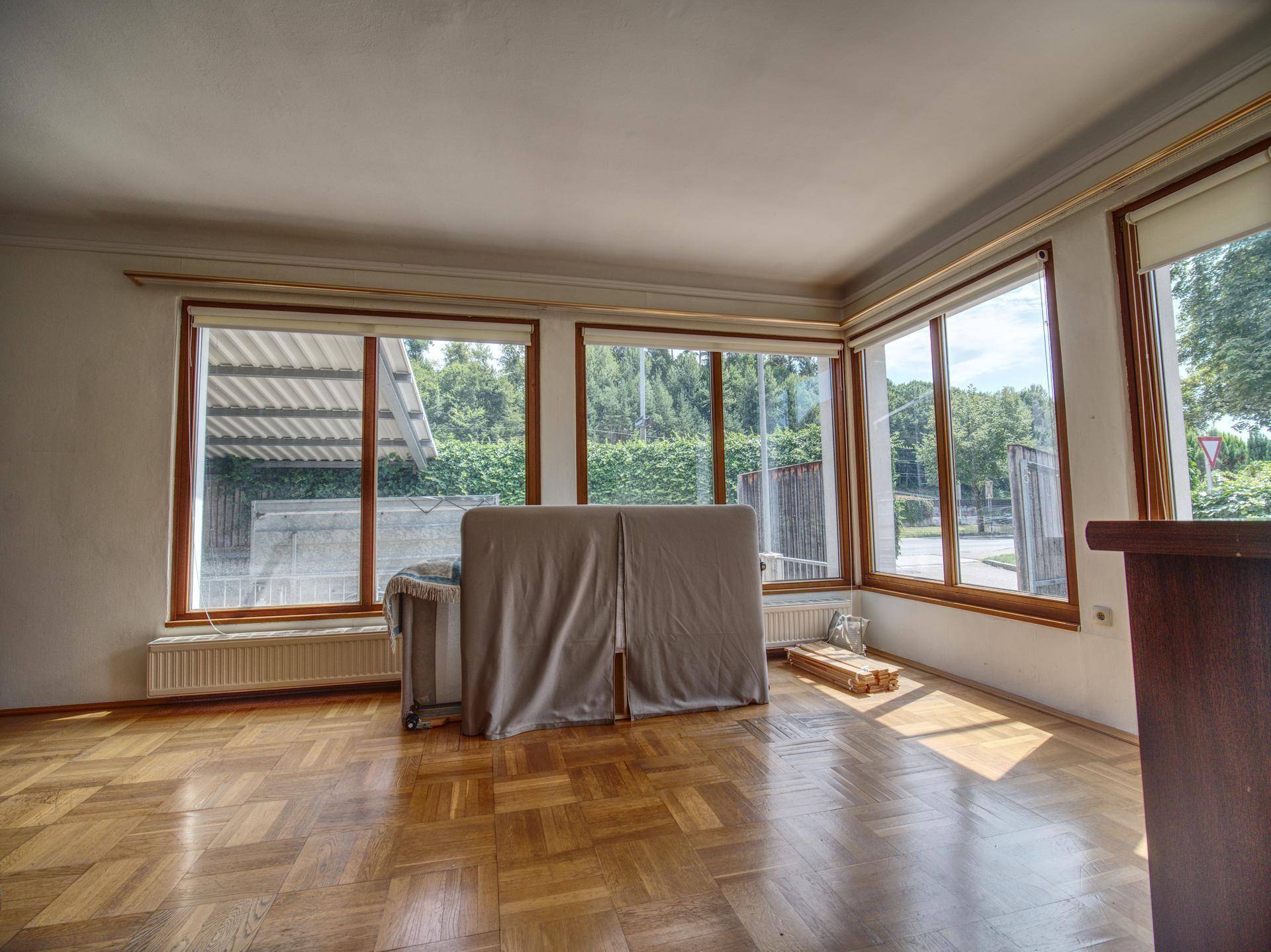Geräumiges Wohnzimmer mit Parkettboden und großen Fenstern, die viel Licht hereinlassen.