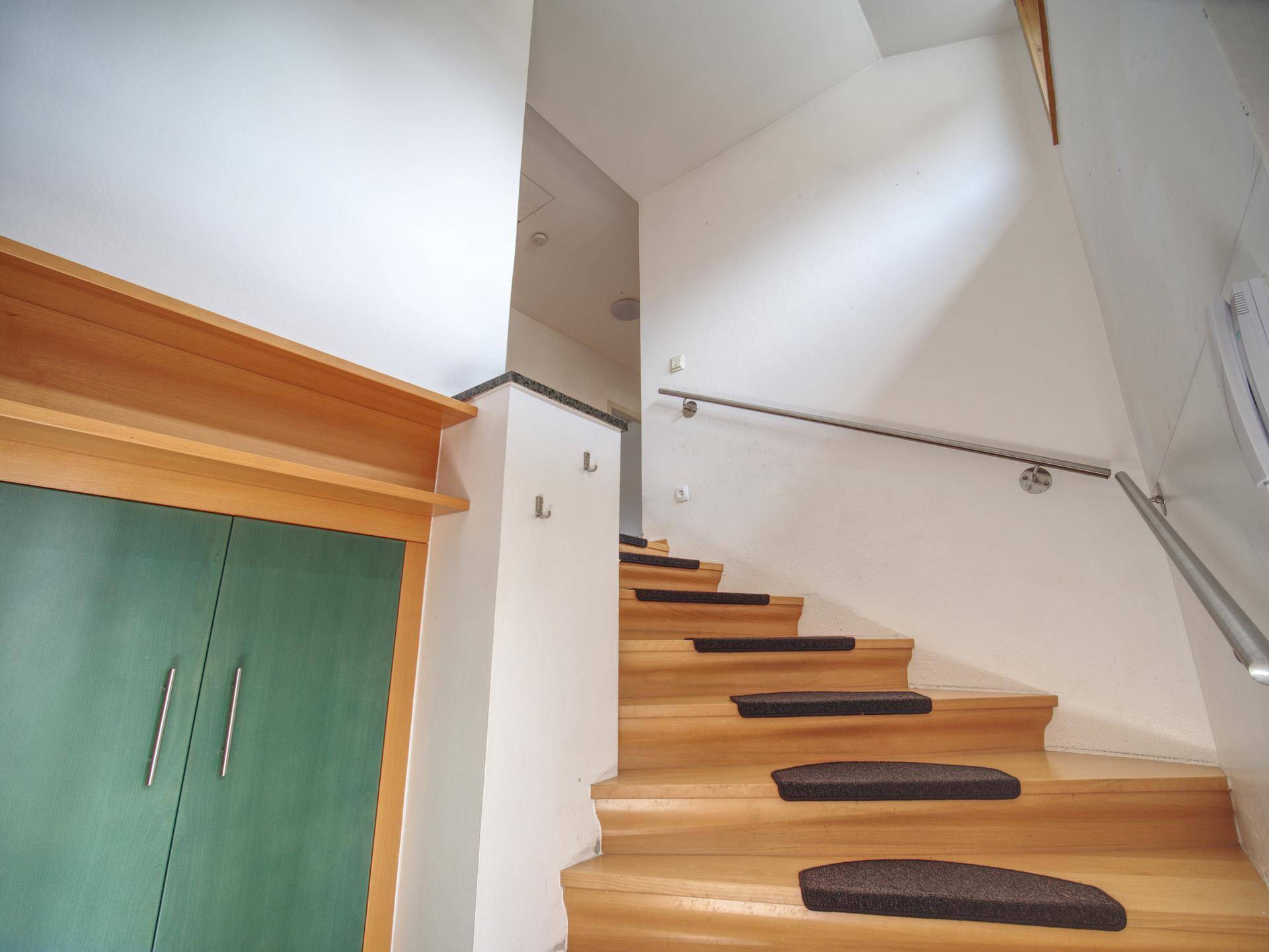 Holztreppe mit Teppichstufen und modernem Edelstahlgeländer, führt in die obere Etage.