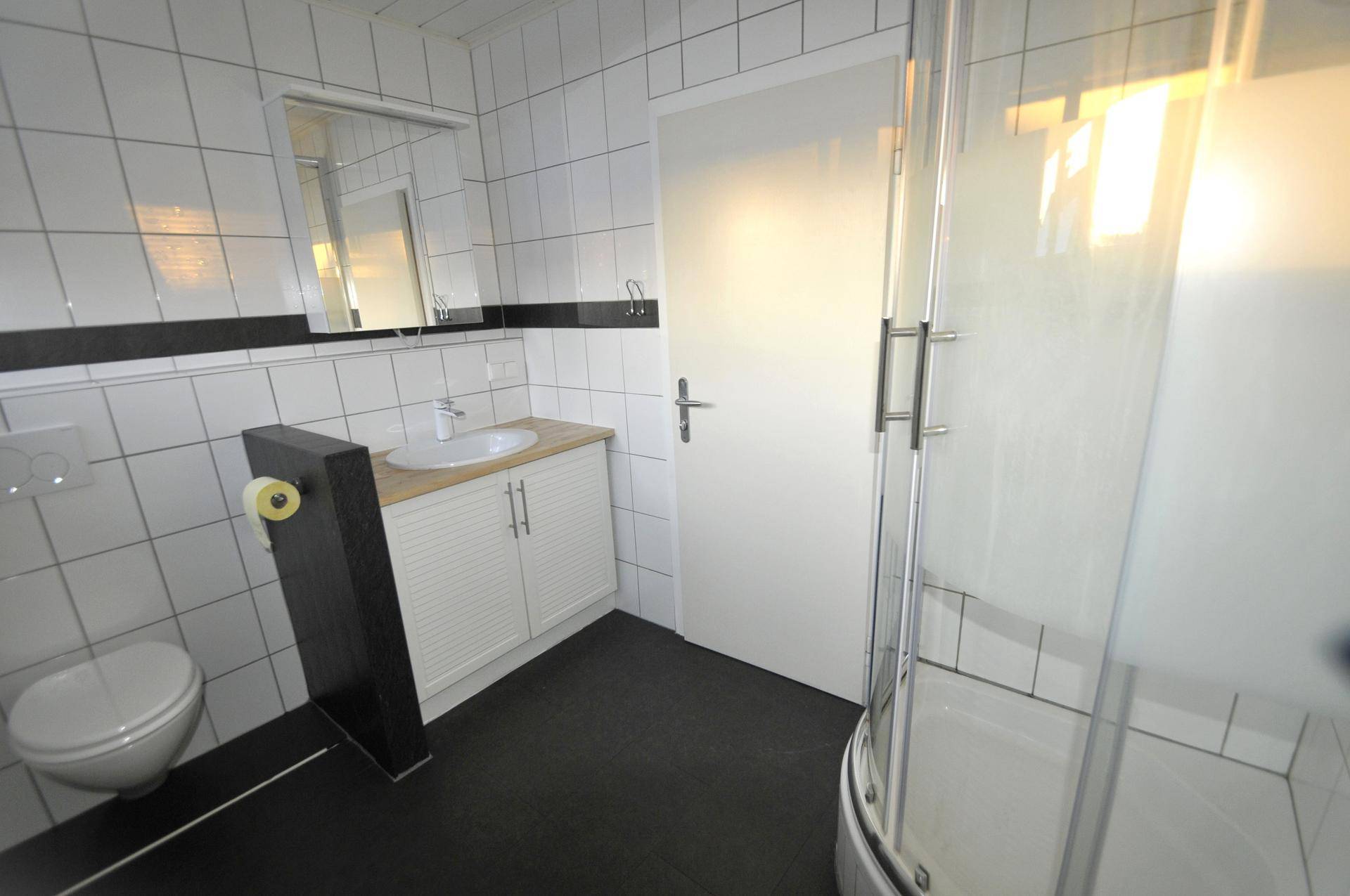 Modernes Badezimmer mit weißen Fliesen, schwarzem Boden, Einzelwaschbecken und Duschkabine.