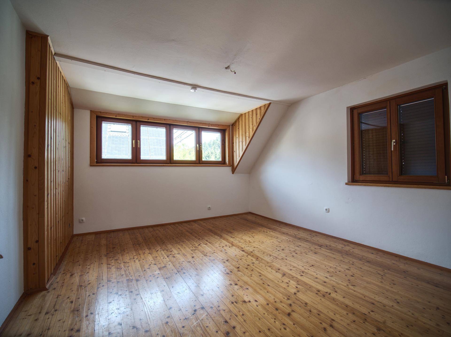 Geräumiges Zimmer im Dachgeschoss mit Holzboden und schrägen Wänden.