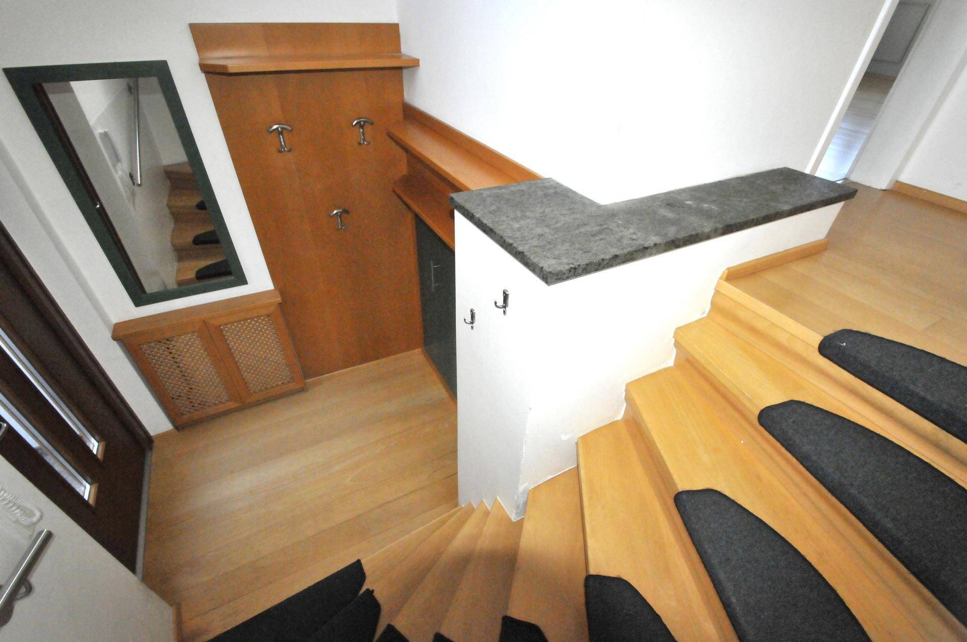Heller Eingangsbereich mit Holztreppe, integrierter Garderobe und einem Spiegel an der Wand.