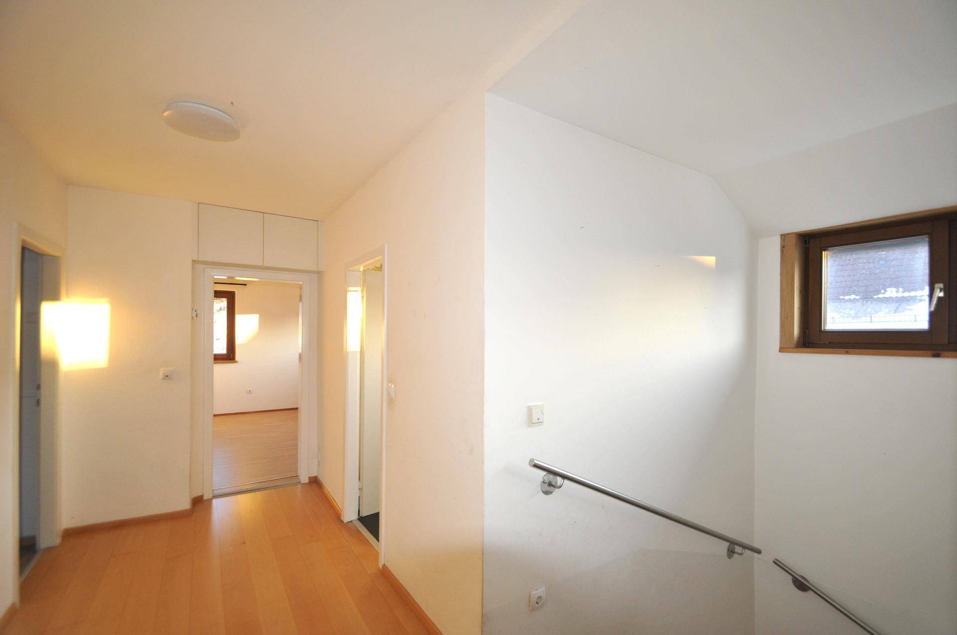 Heller Flur im Obergeschoss mit Holzboden, weißen Wänden und einem kleinen Fenster für natürliches Licht.