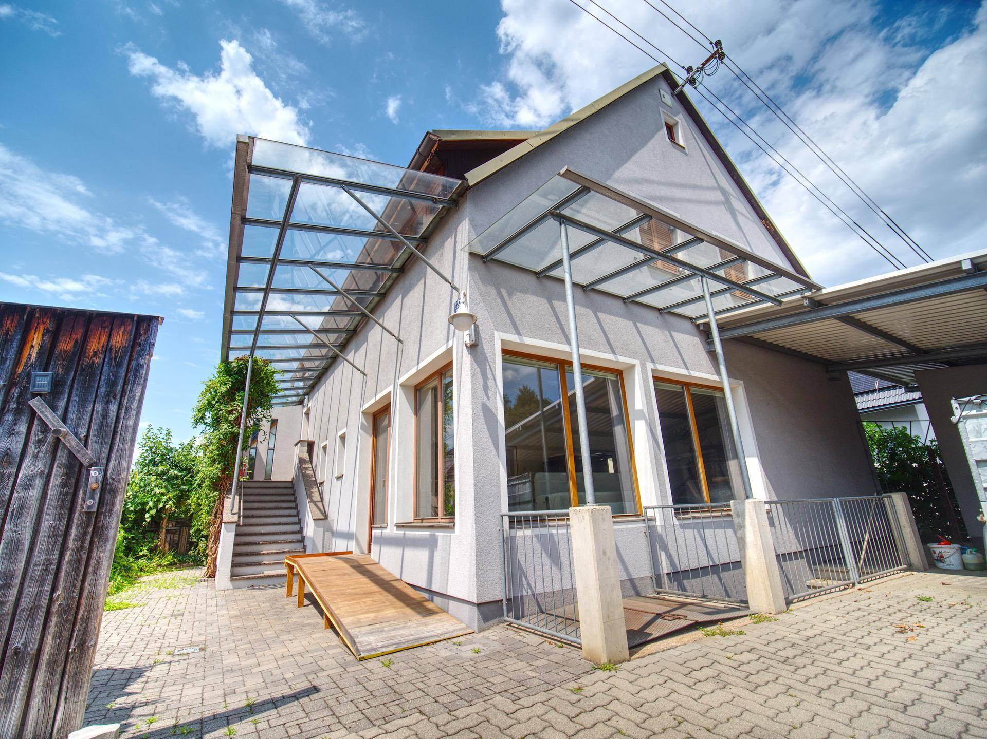 Seitenansicht des Hauses mit barrierefreier Rampe und einer modernen Glasüberdachung.