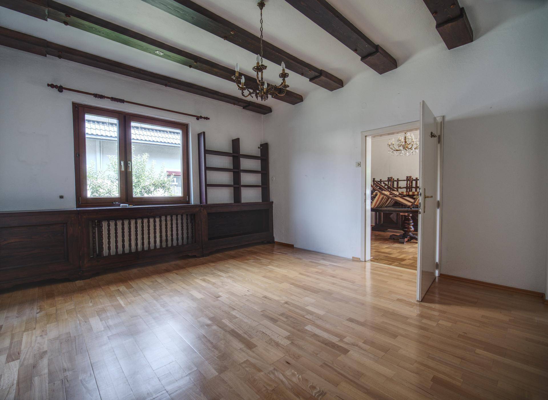 Wohnraum mit Holzbalkendecke, Parkettboden und einem großen Fenster.