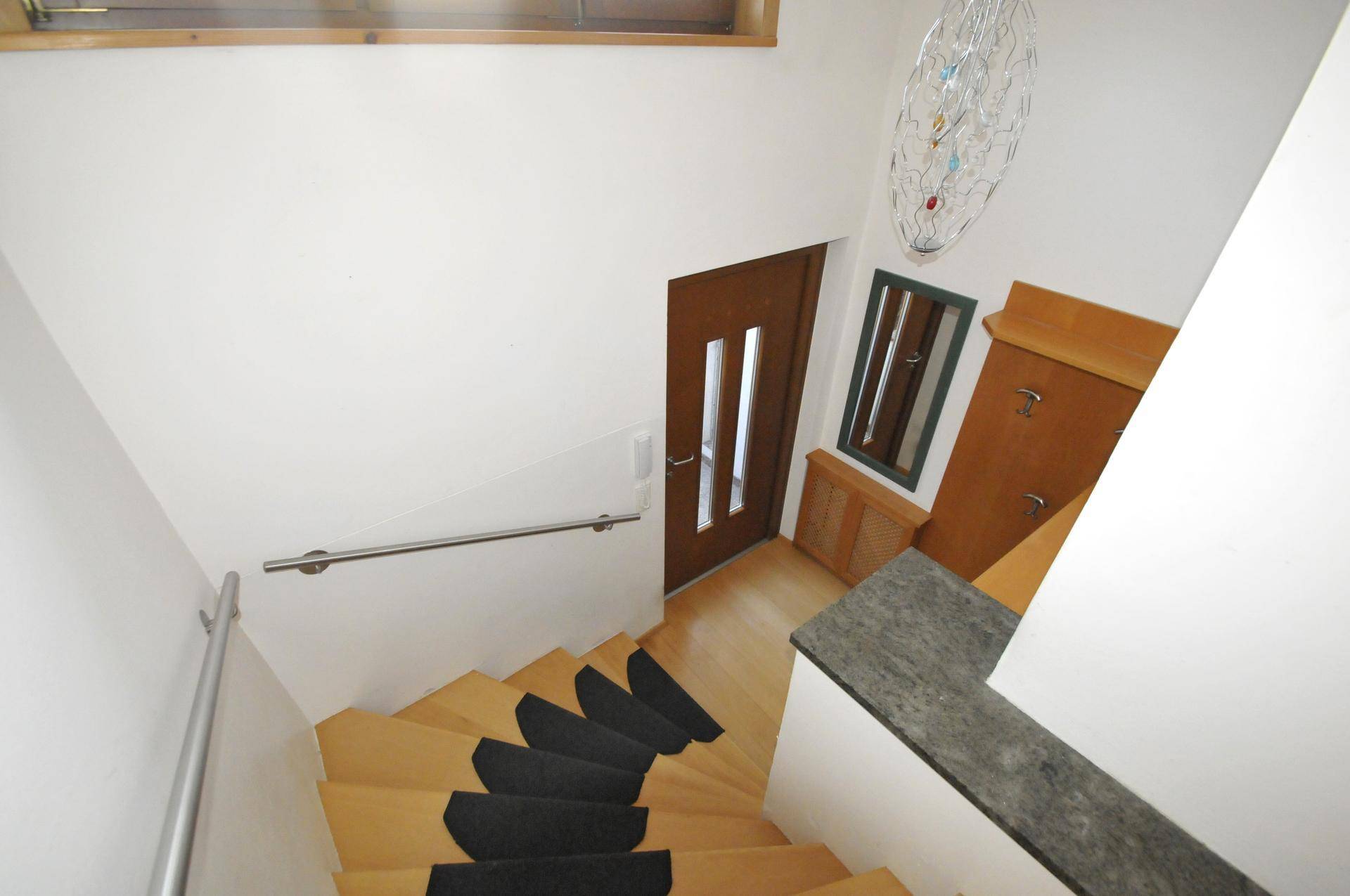 Holztreppe mit Handlauf und Garderobe in einem hellen Flurbereich.