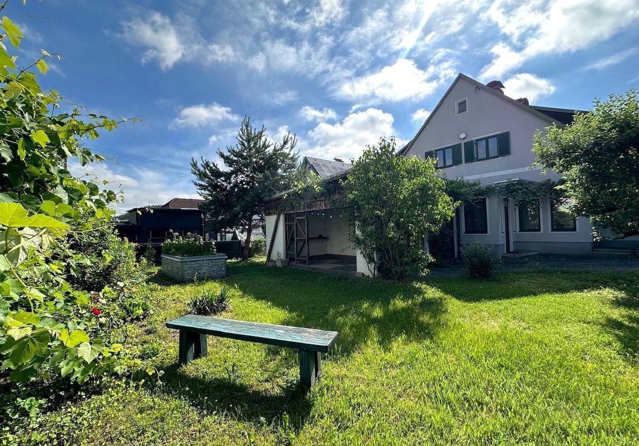 Großer Gartenbereich mit Rasenfläche, einer Holzbank und einem überdachten Außenbereich am Haus.