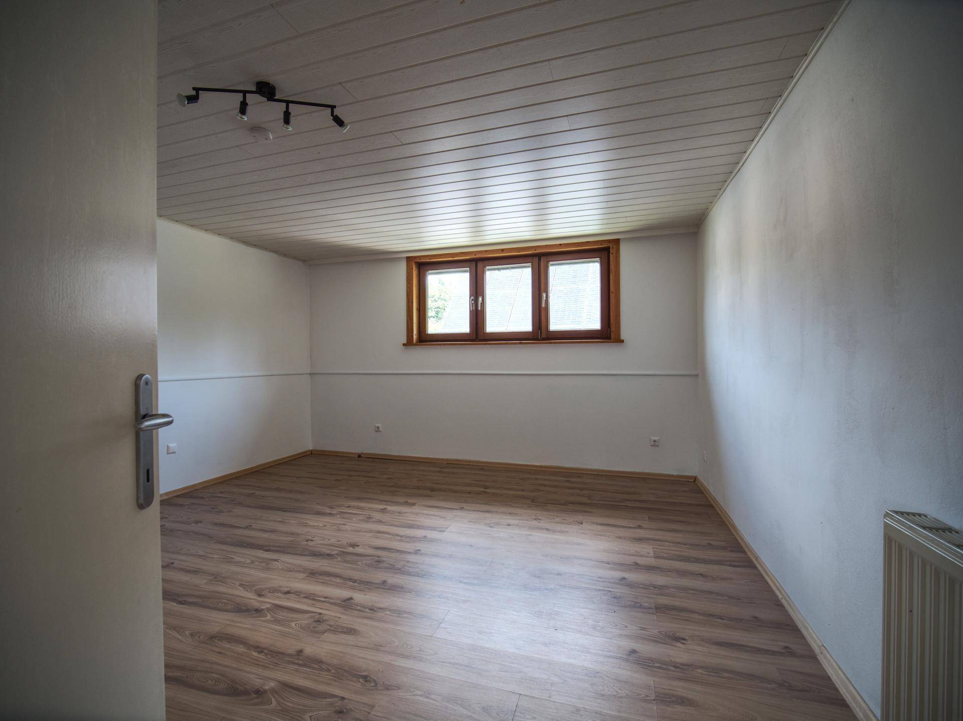 Helles Zimmer mit Laminatboden und Fenster, ideal als Schlaf- oder Arbeitszimmer.