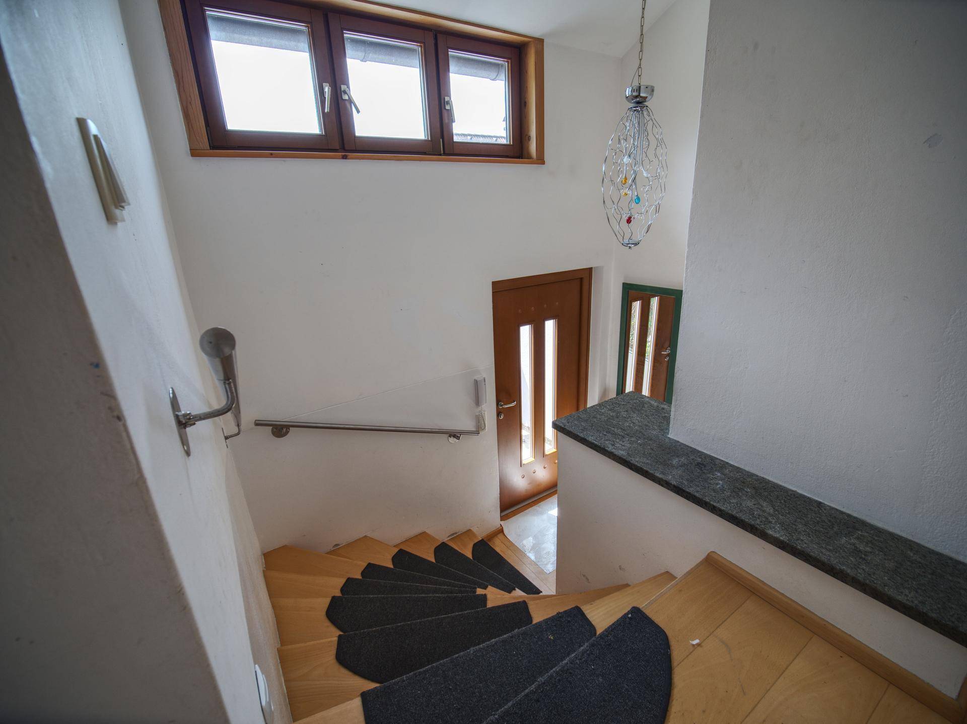 Wendeltreppe aus Holz mit Teppichstufen und Blick auf den Eingangsbereich.