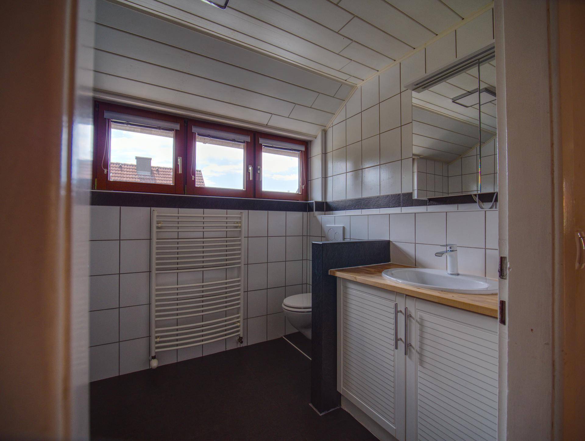 Badezimmer mit weißen Fliesen, Waschtischunterschrank und beheiztem Handtuchhalter.