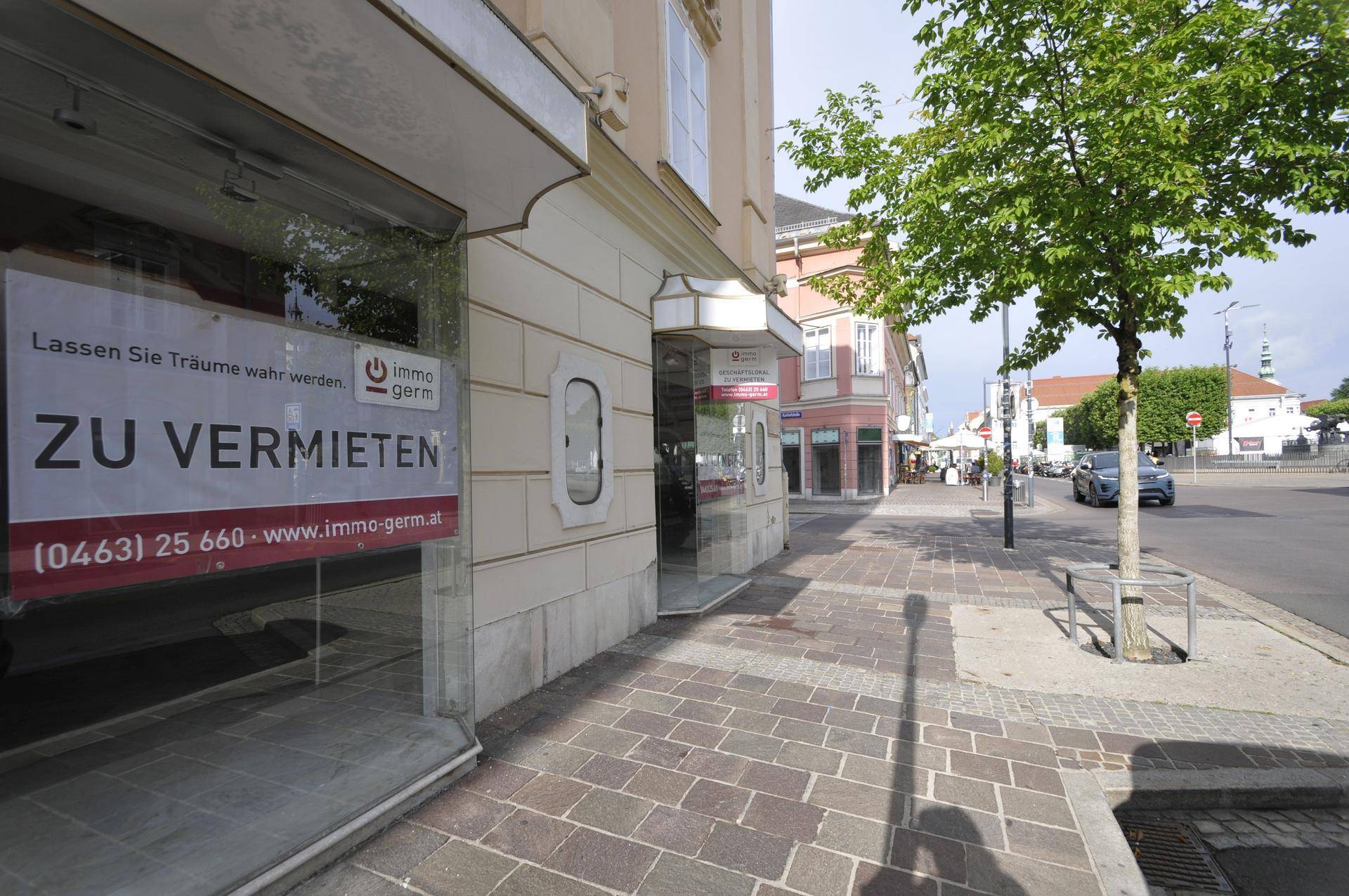 Blick auf die Ladenfronten des Gebäudes mit einem 'Zu vermieten'-Schild im Schaufenster.