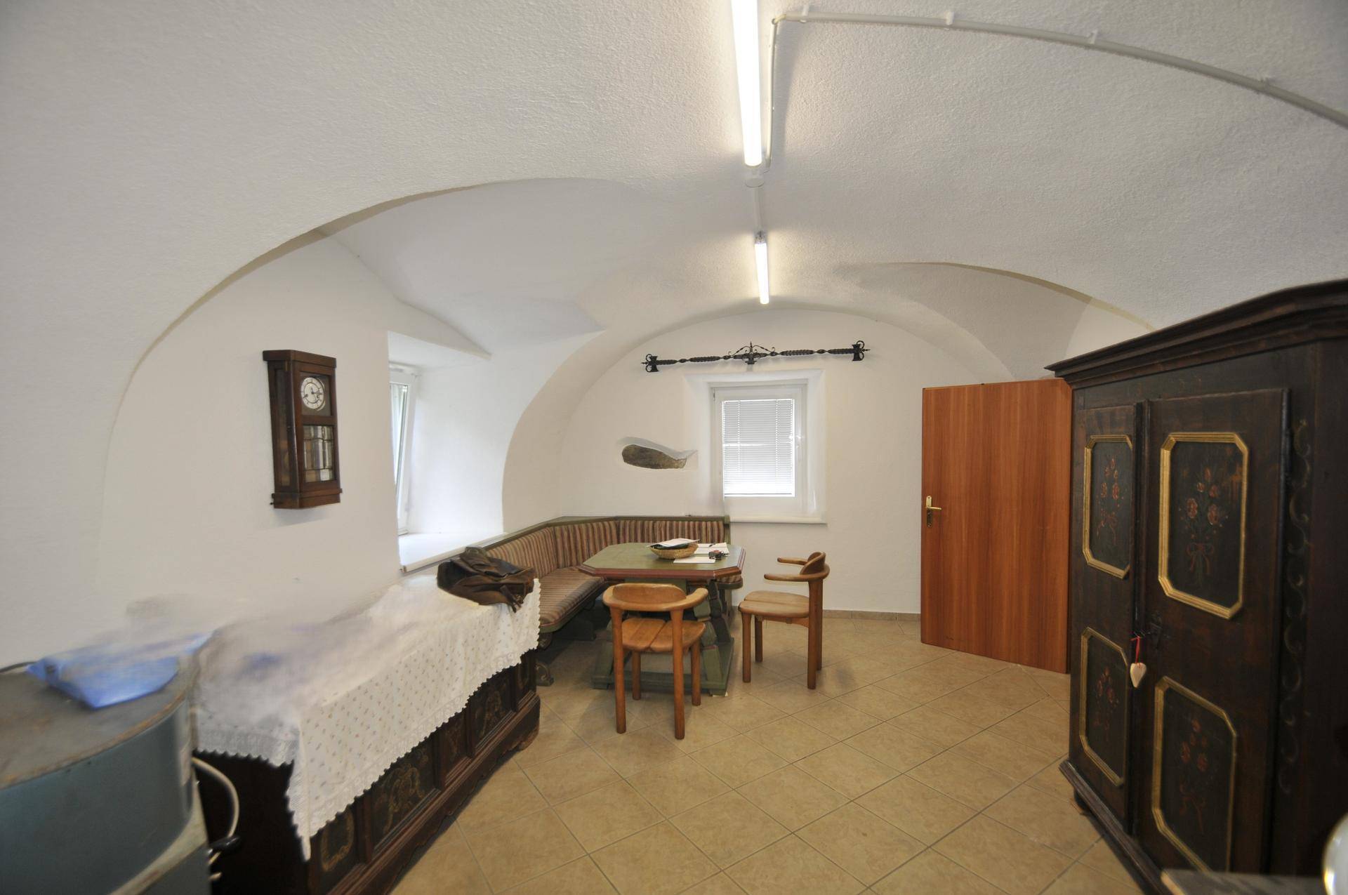 Heller Raum mit weißem Gewölbe, Fliesenboden und traditioneller Eckbankgruppe.
