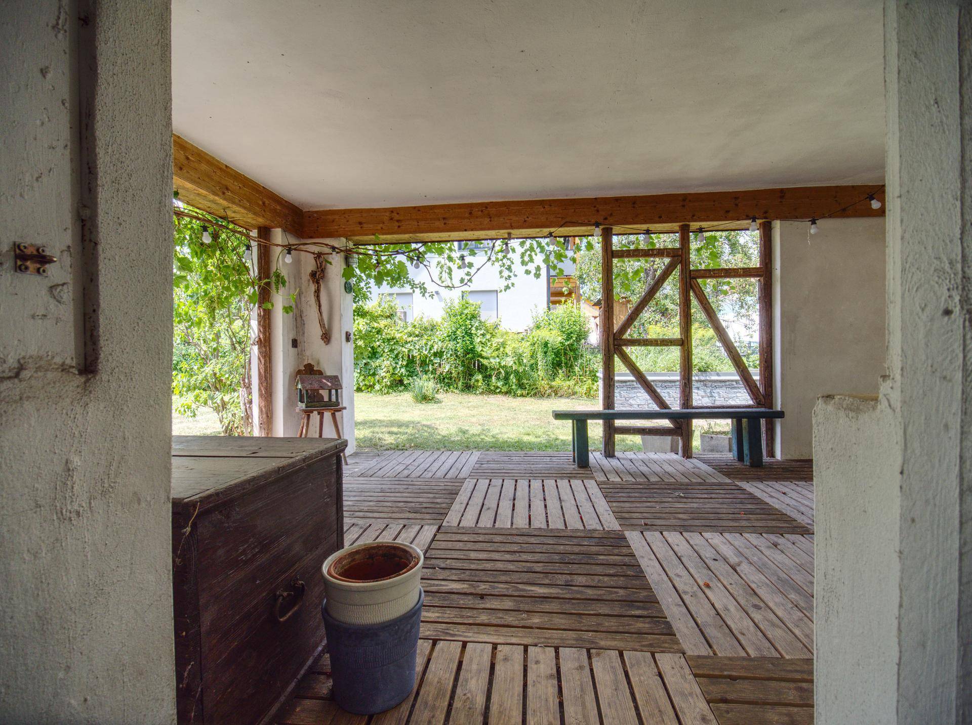 Überdachte Terrasse mit rustikalem Holzboden und Blick in den weitläufigen Garten.