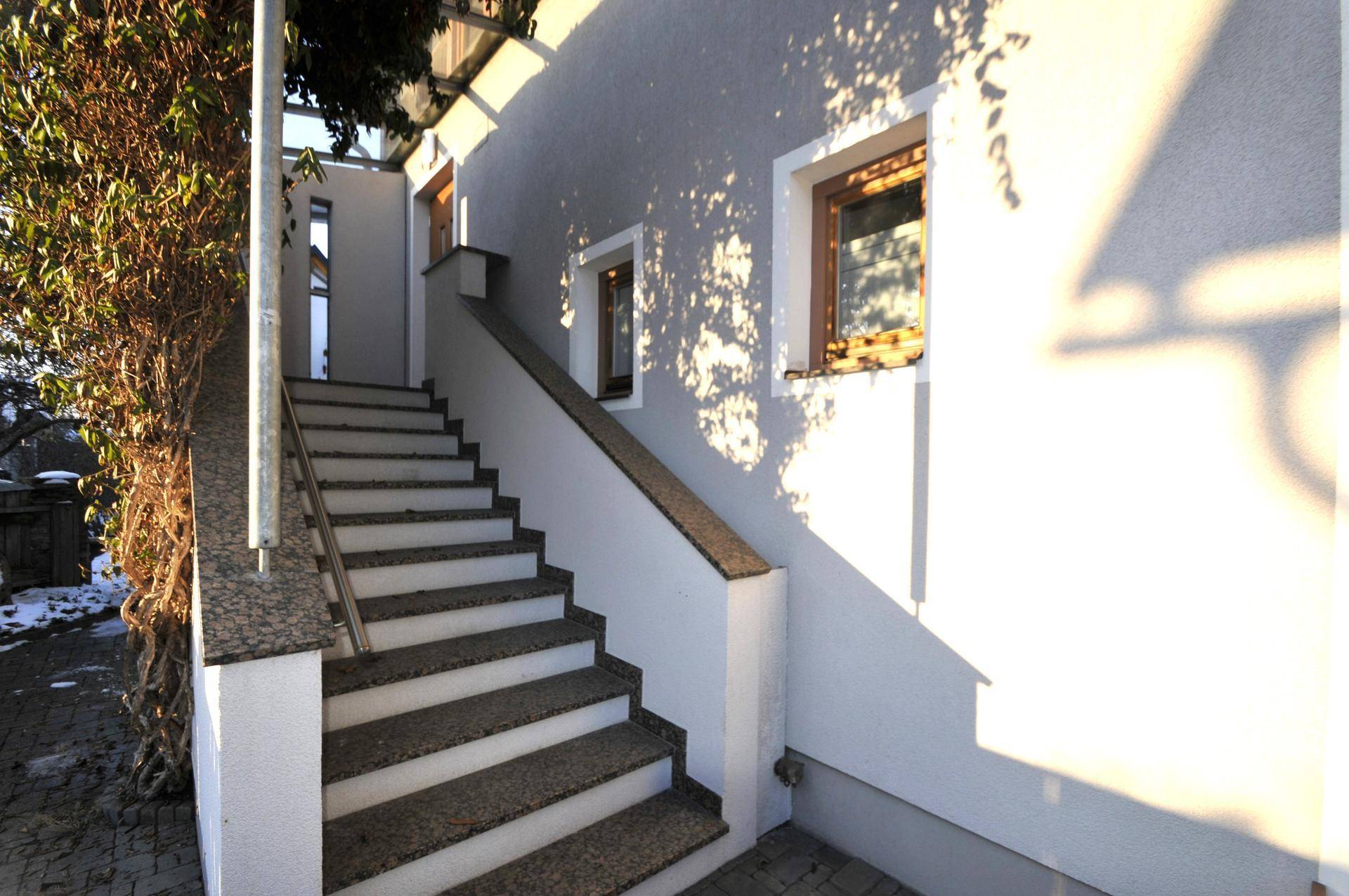 Außentreppe mit Geländer und Fensterfront an der grauen Hausfassade.
