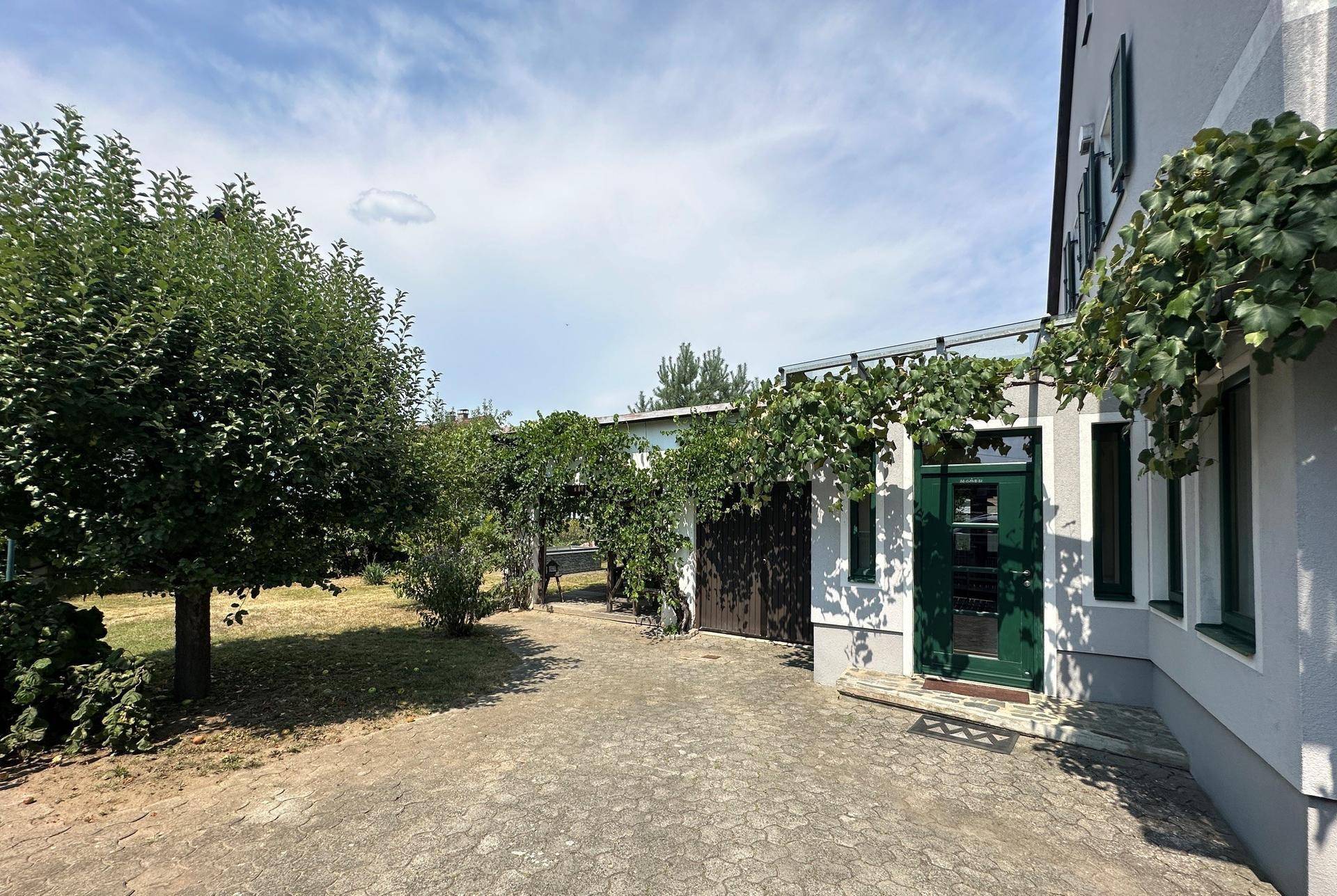 Gepflasterter Hofbereich neben dem Haus mit üppigem Grün und Zugang zum Garten.