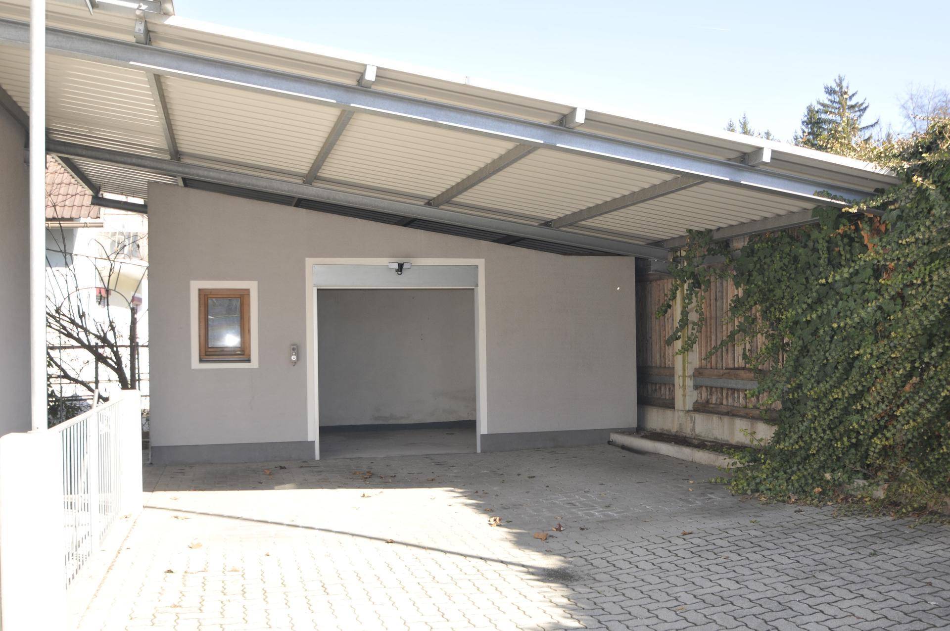 Geräumiger Carport und separate Garage mit offenem Tor, ideal für mehrere Fahrzeuge.