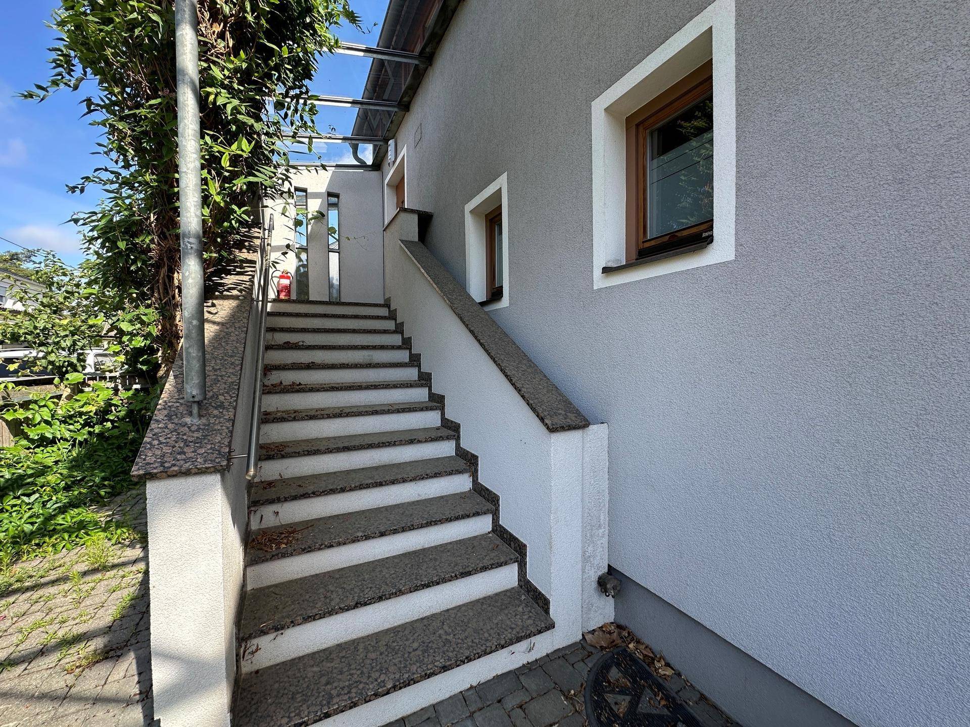 Außentreppe mit Steinstufen und einem Geländer, die zu einem oberen Eingang des Hauses führt.