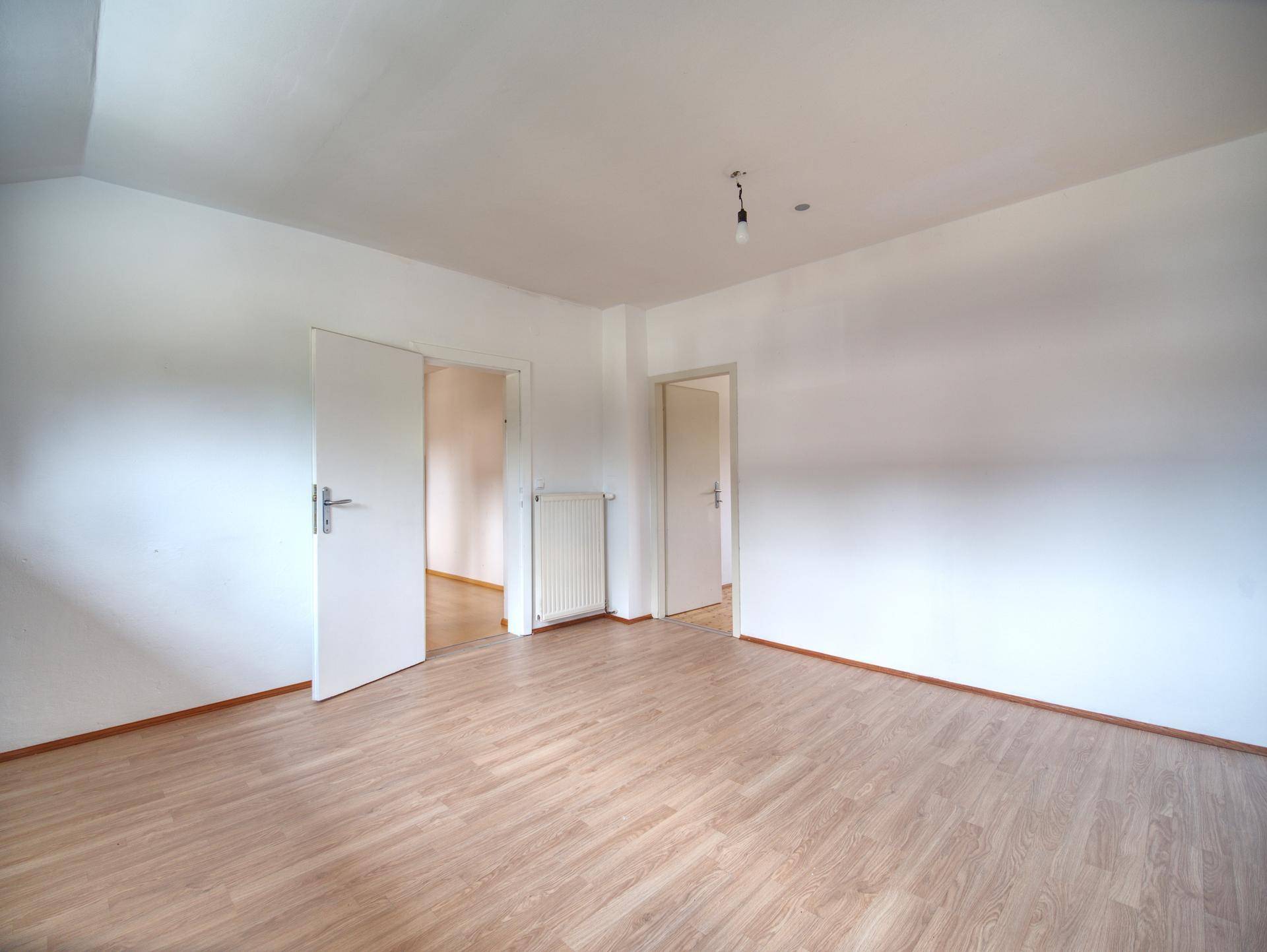 Leeres Zimmer mit hellem Laminatboden und weißen Wänden, bereit zur individuellen Gestaltung.