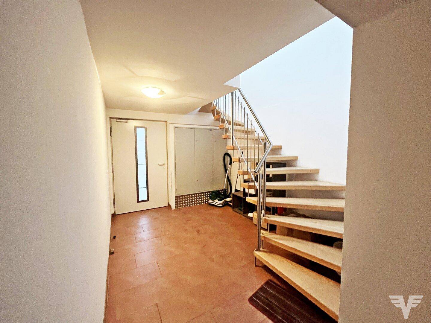 Heller Flur mit Holztreppe und Metallgeländer, der zu den oberen Etagen führt.