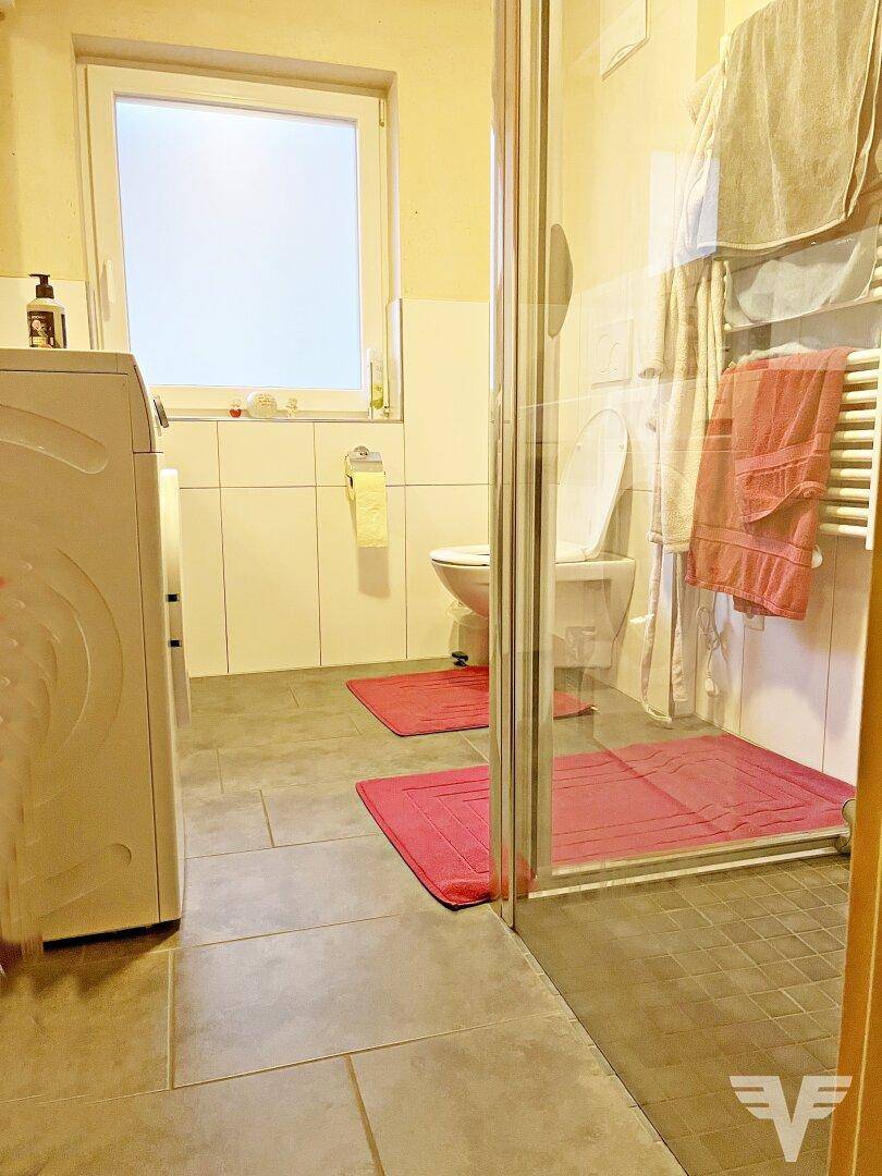 Badezimmer mit Duschkabine, WC, Waschmaschine und Fenster für Tageslicht.