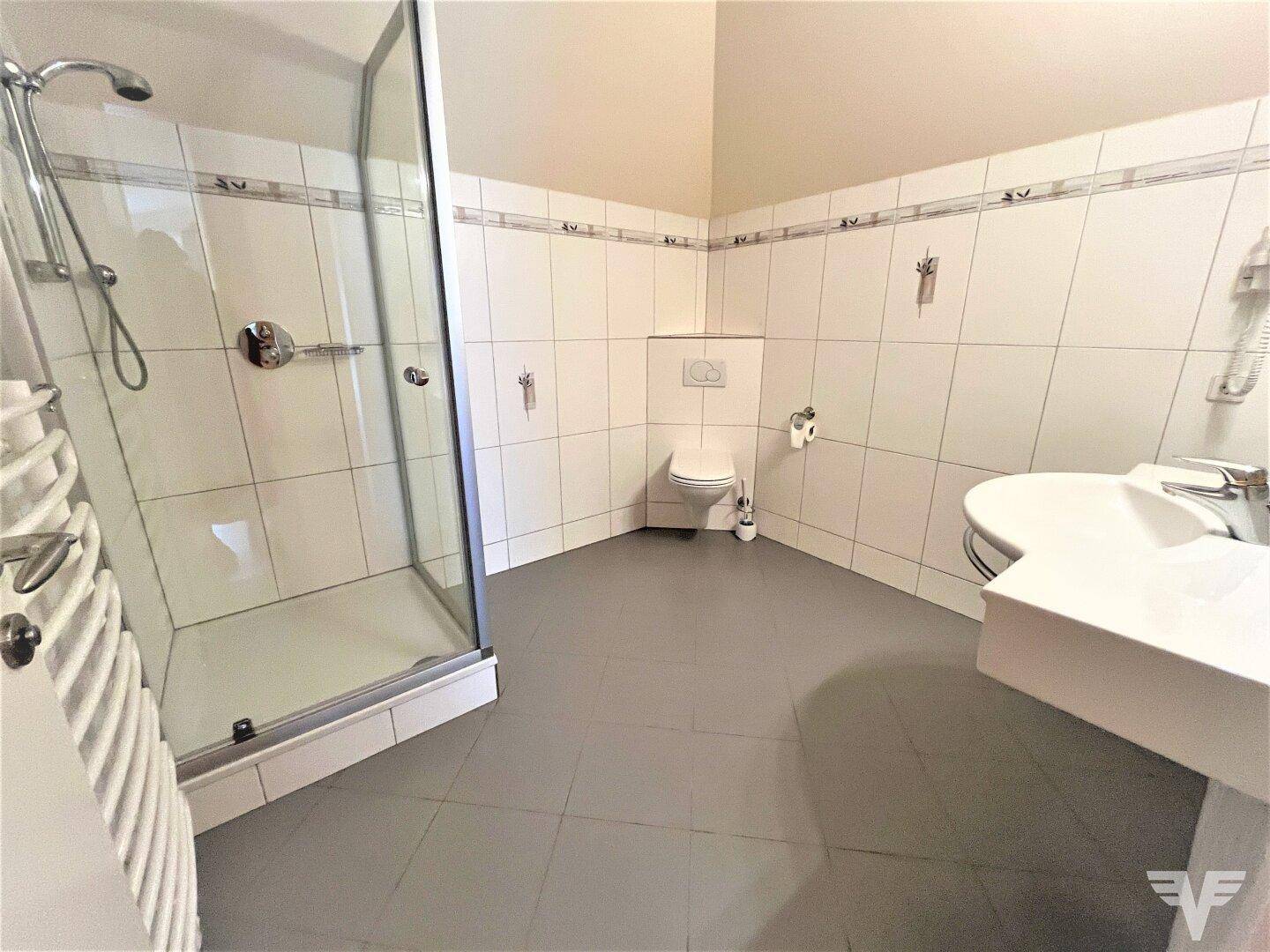 Badezimmer mit weiß gefliesten Wänden, Duschkabine, WC und beheiztem Handtuchhalter.