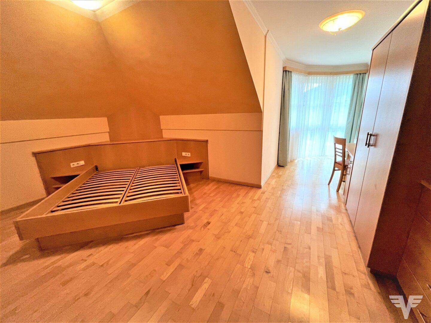 Schlafzimmer im Dachgeschoss mit Holzbett, schräger Decke und großem Fenster.