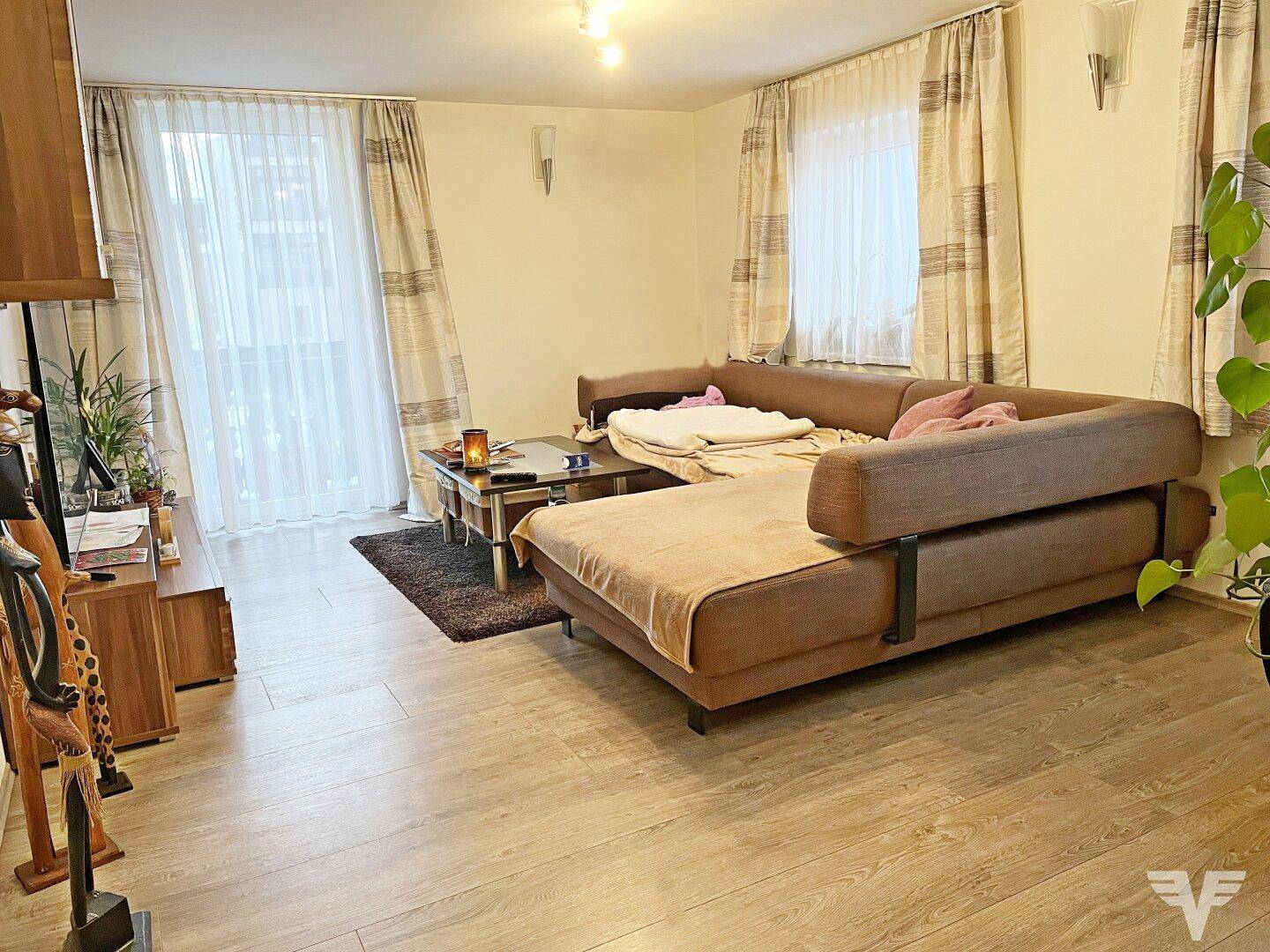 Helles Wohnzimmer mit L-förmigem Sofa, Laminatboden und großem Fenster mit Zugang zu einem Balkon.