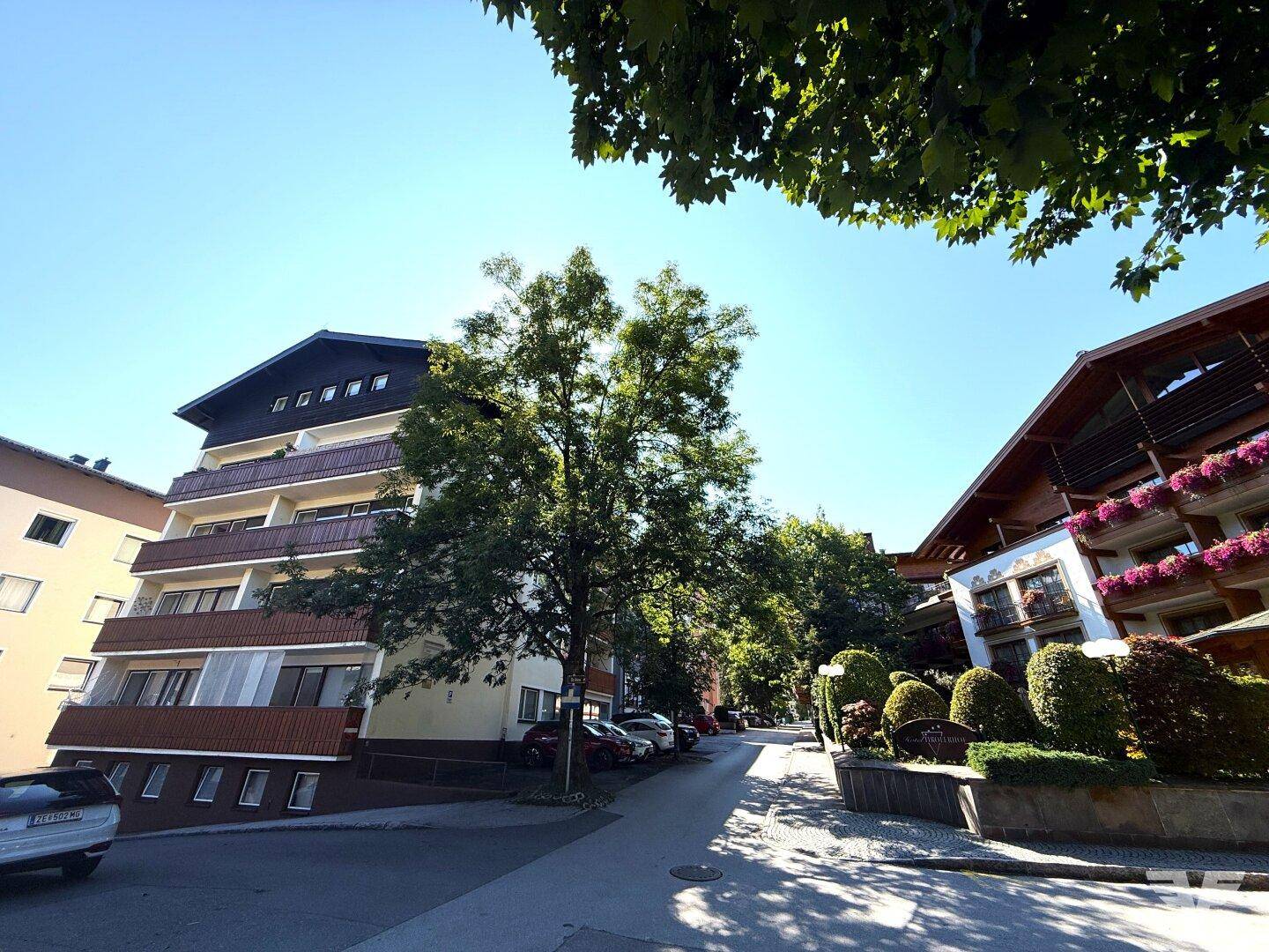 Blick auf eine ruhige Wohnstraße mit Mehrfamilienhäusern und viel Grün an einem sonnigen Tag.