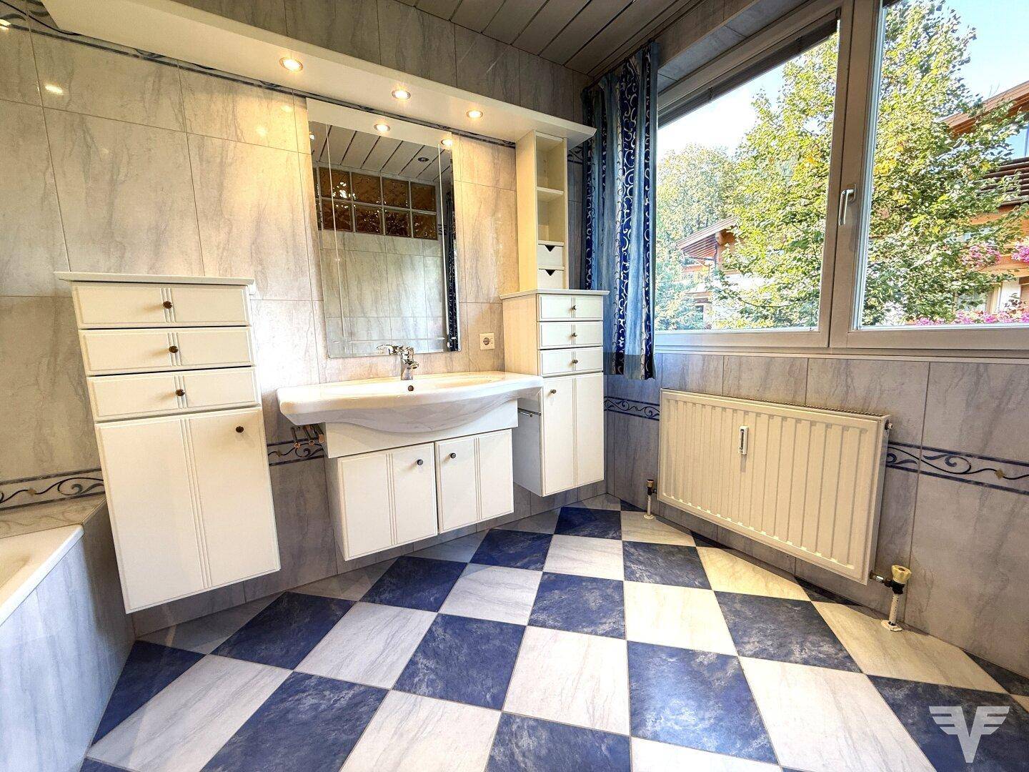 Badezimmer mit blau-weiß karierten Fliesen, Fenster und einem Waschtisch mit Spiegelschrank.