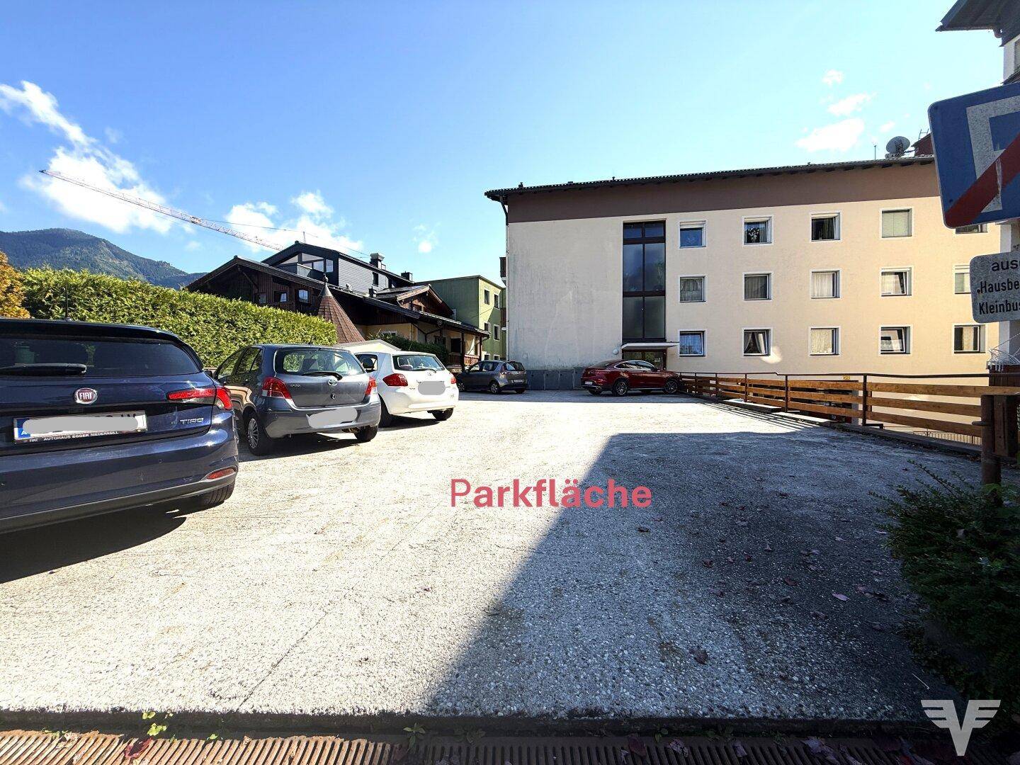 Offener Parkplatz im Freien mit mehreren Fahrzeugen und angrenzendem Wohngebäude.